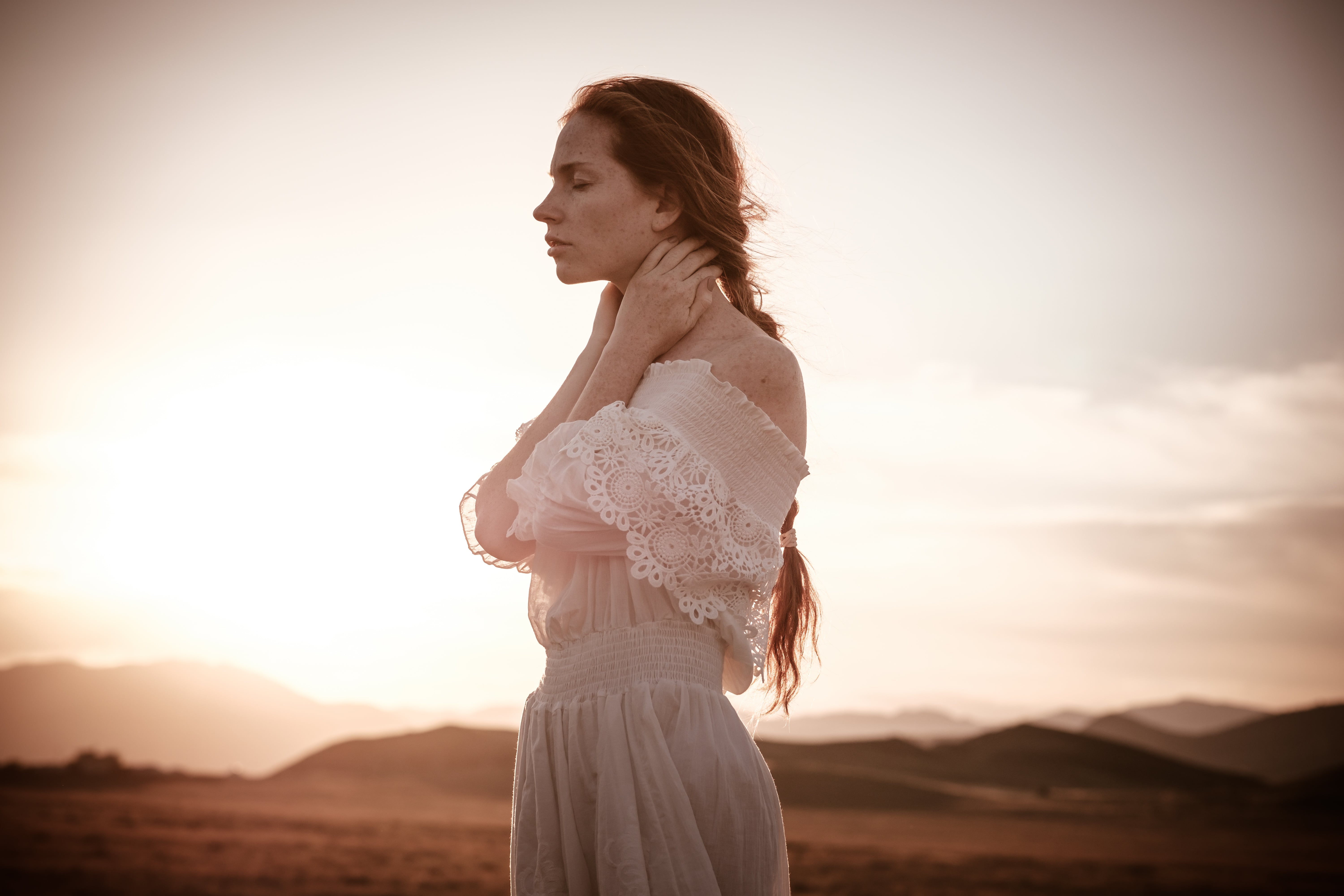 redhead woman in 
a white dress standing in wheat field at sunset