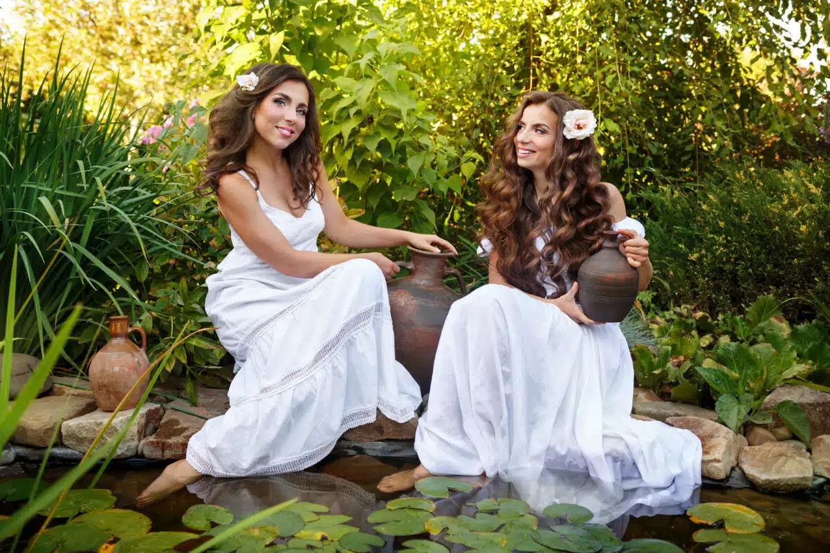 Two fairies in white dresses draw water from a pond
