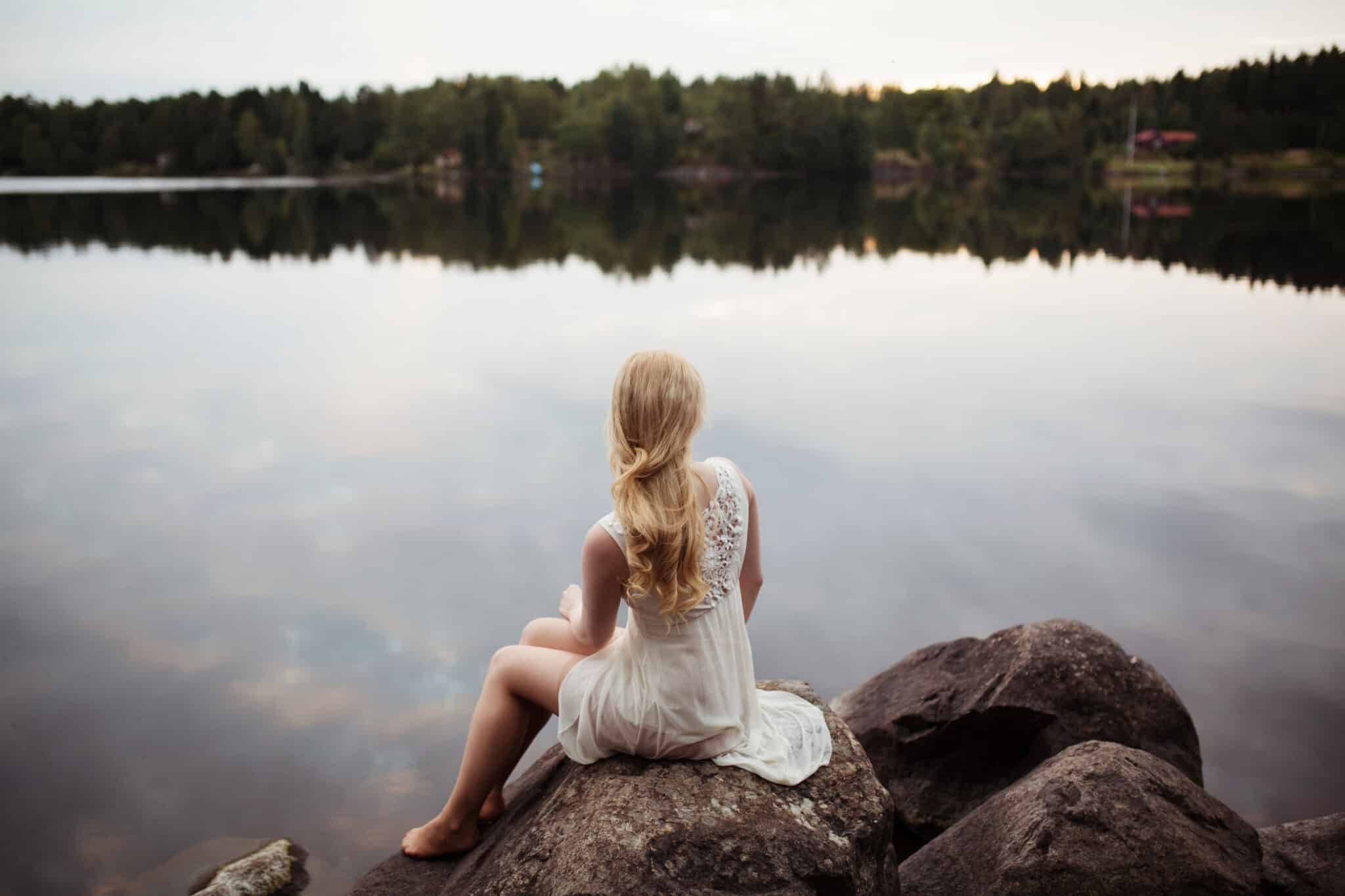 woman sitting on the edge of a lake