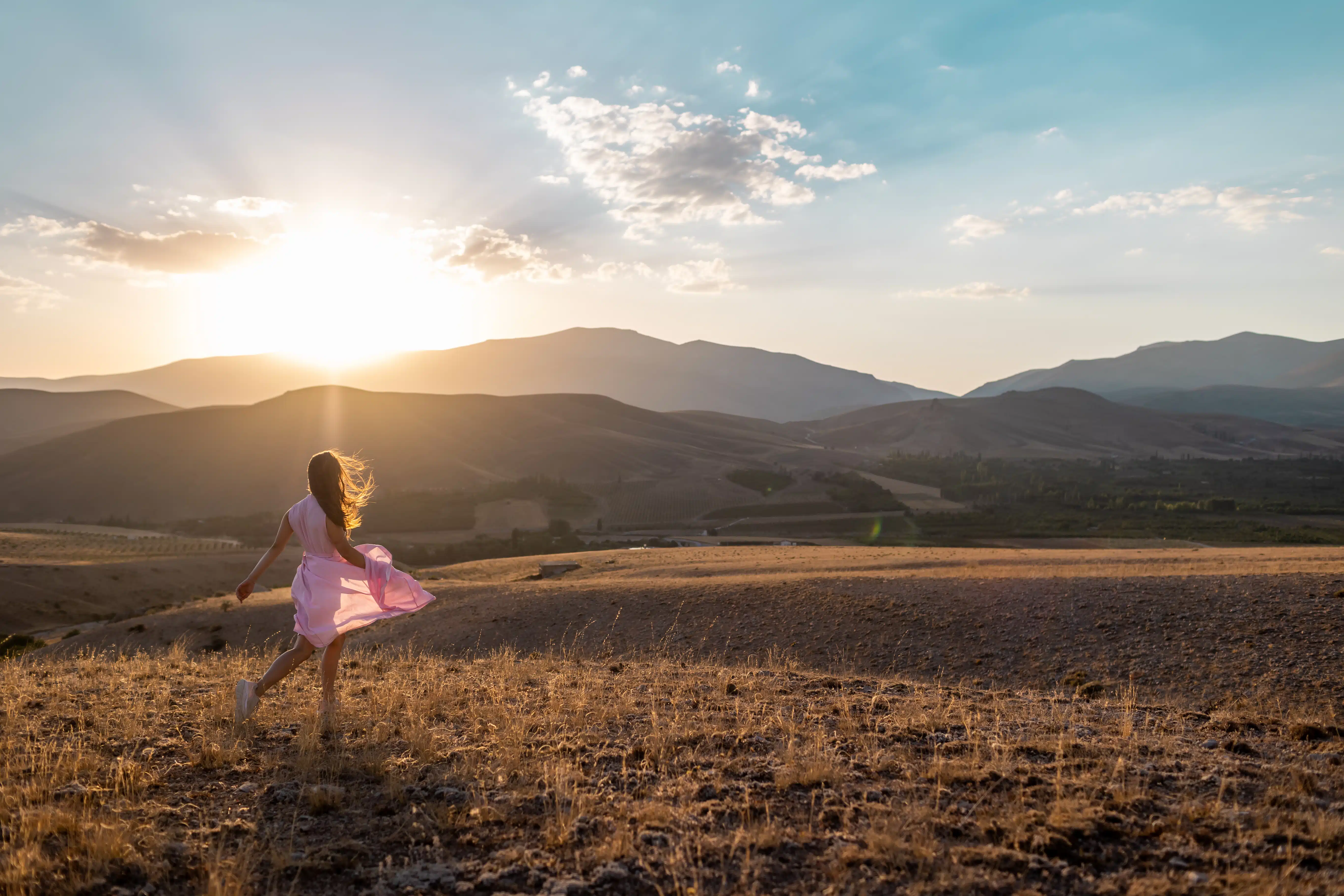 a young woman in a pink dress walks across the field at sunrise