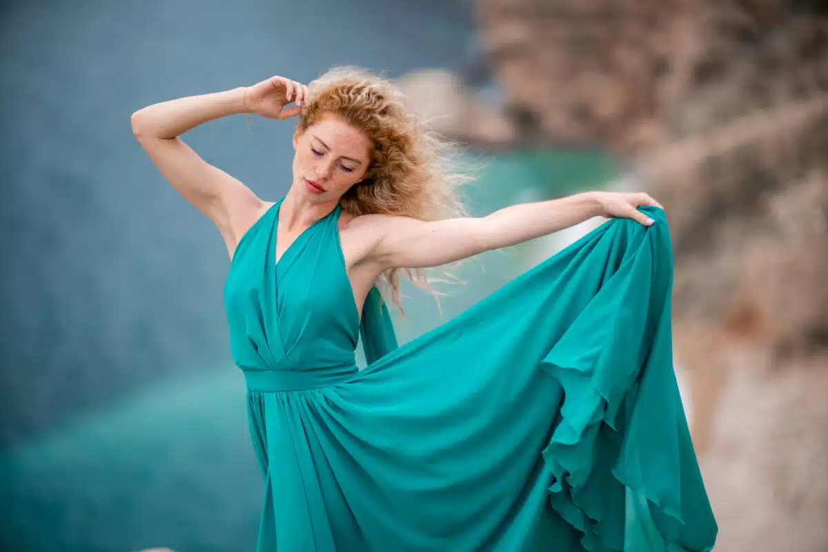 A woman in an emerald dress with long silk wings in a flowing dress