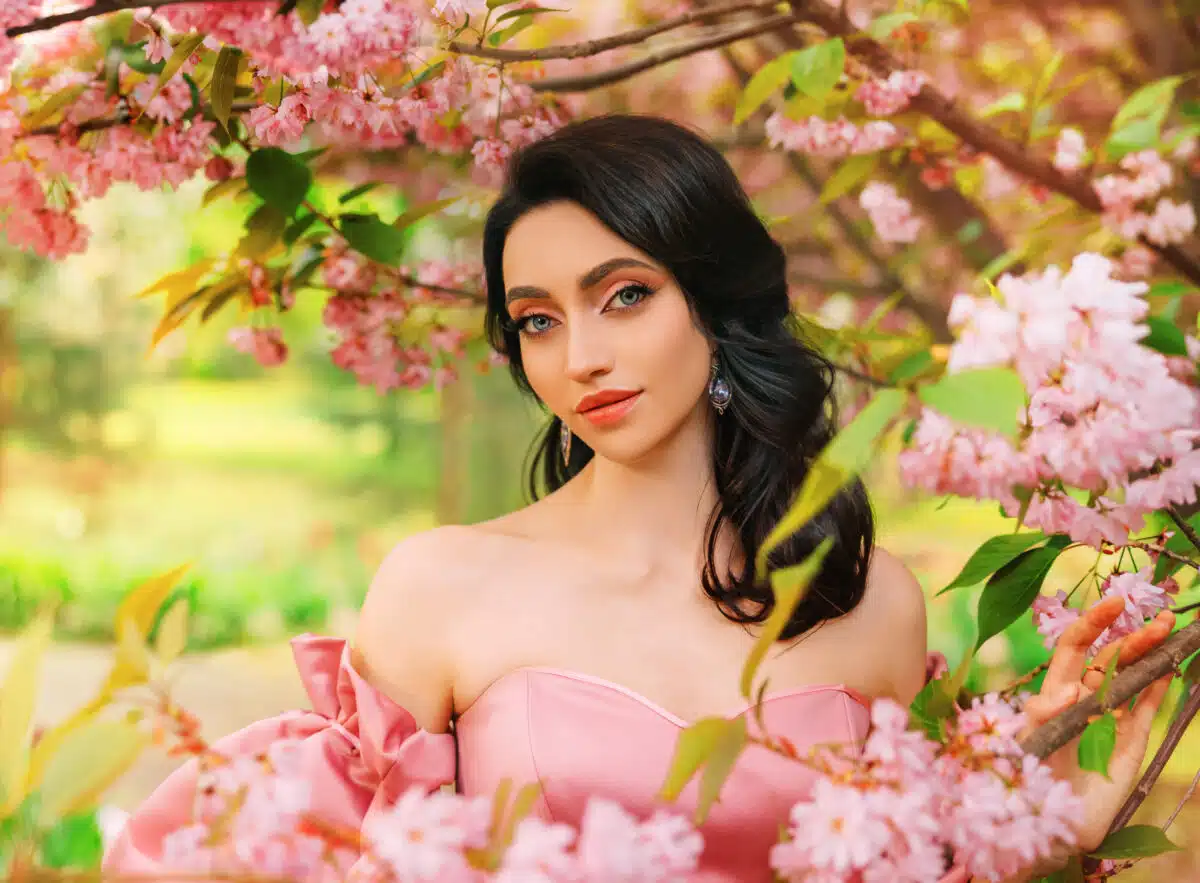 Portrait Fantasy girl princess in blooming spring garden flowers sakura tree green grass. Happy woman queen beauty face Lady in romantic pink sexy dress bare open shoulders vintage old style