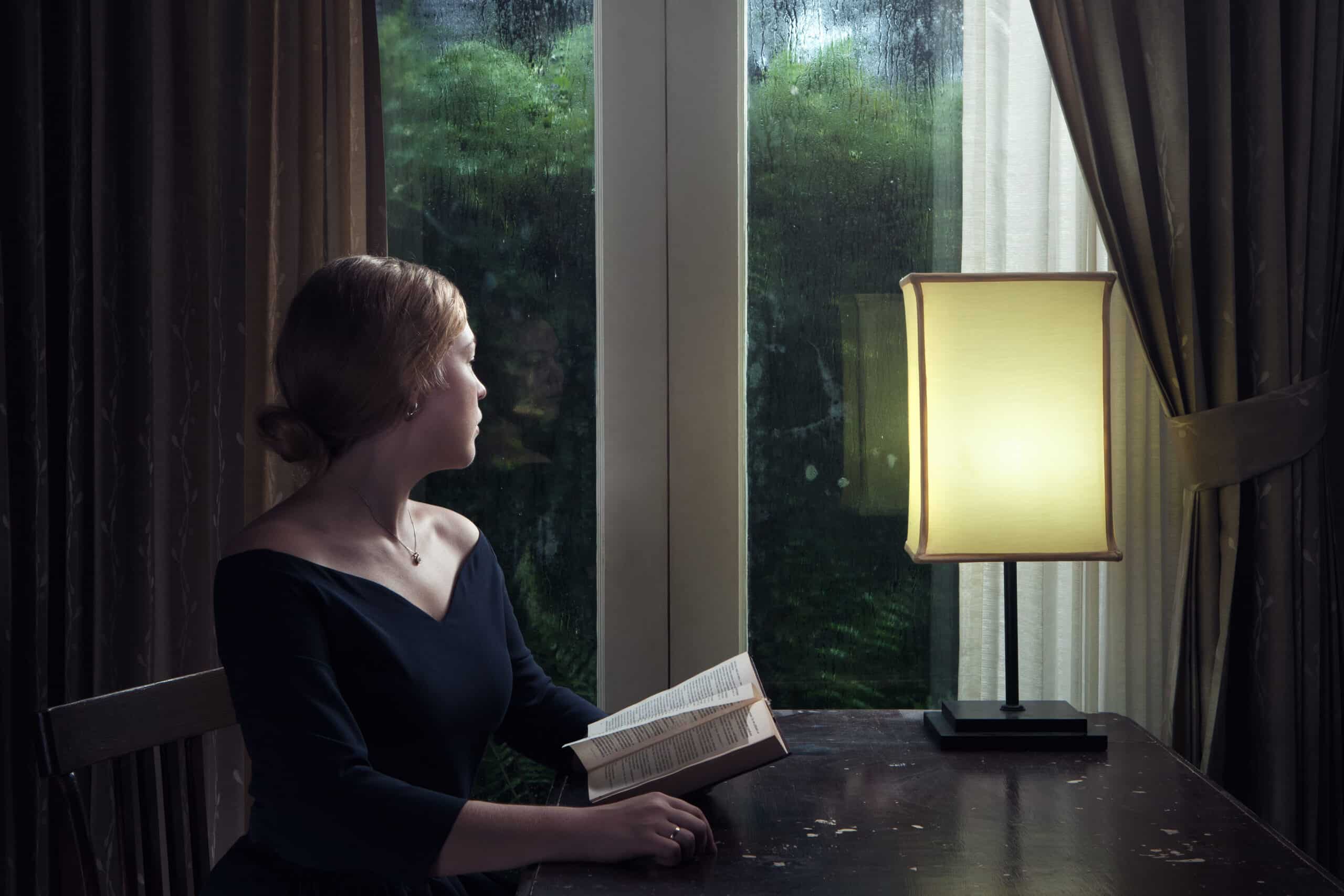 portrait of young woman with book sitting by the window