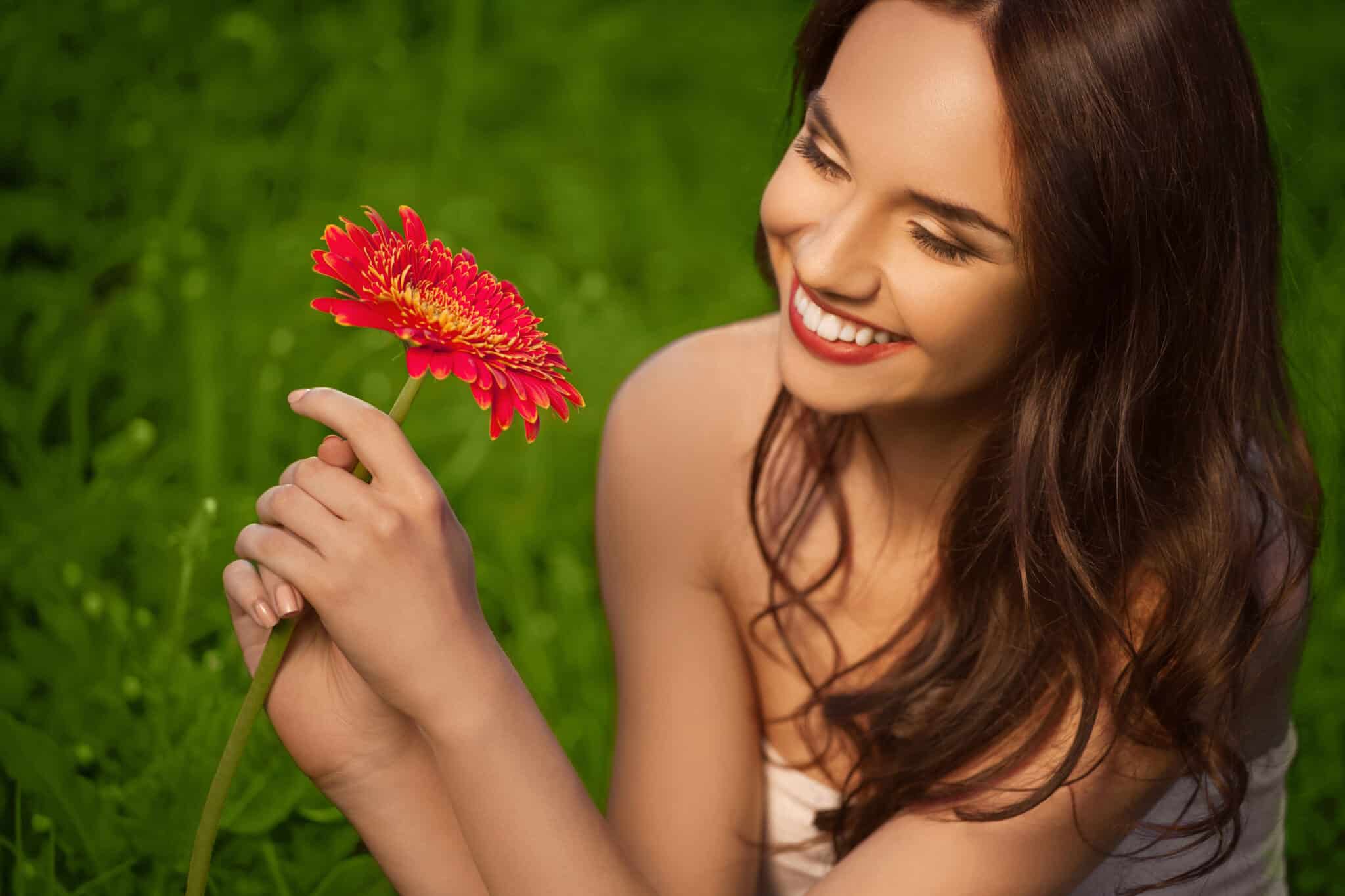 pretty and happy young woman holding a red daisy enjoying nature
