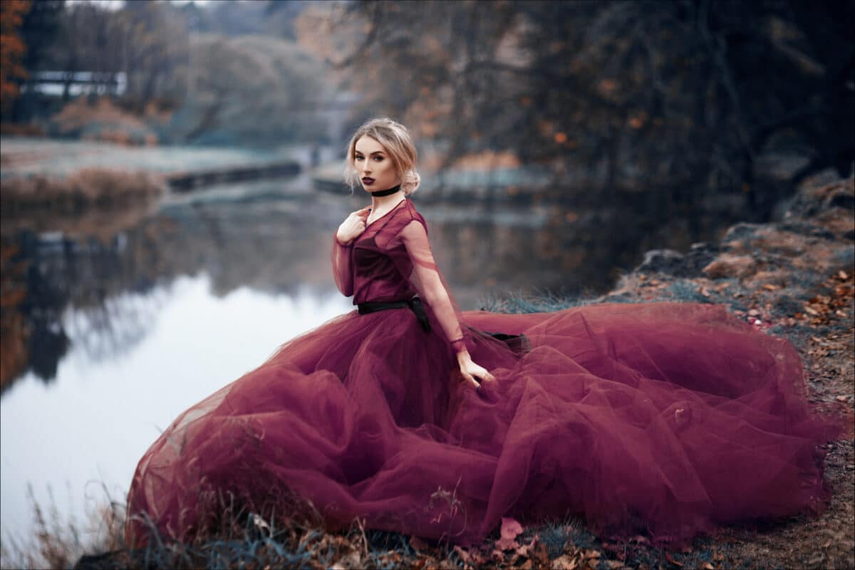Young fragile girl in a red long dress on the background of the forest like a fairytale