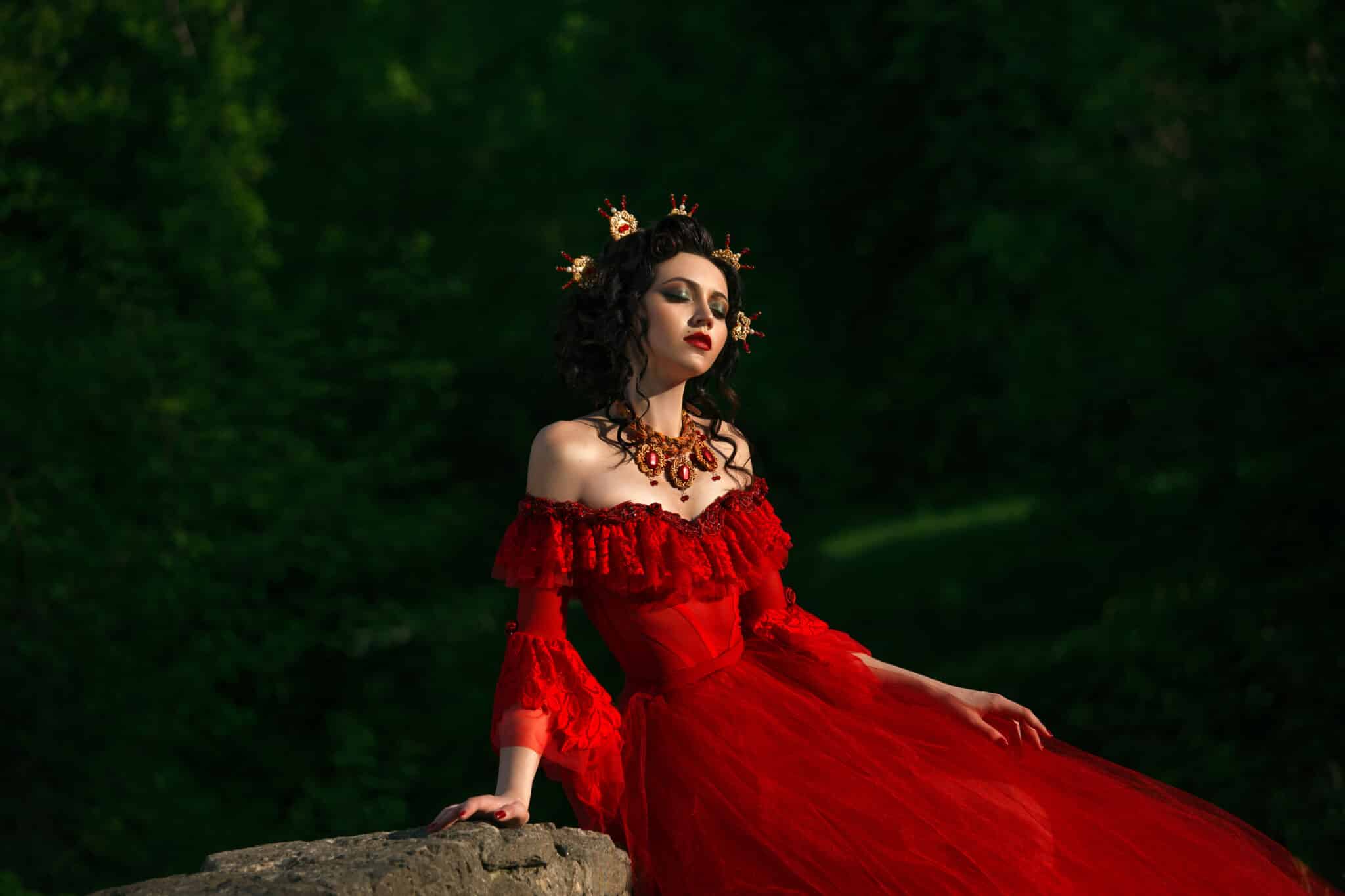 The young Countess in a luxurious red dress sitting of nature.