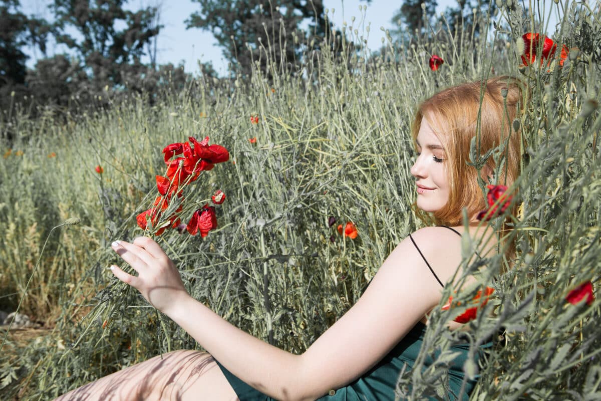 a young beautiful lady sitting on the ground amidst poppies and grass