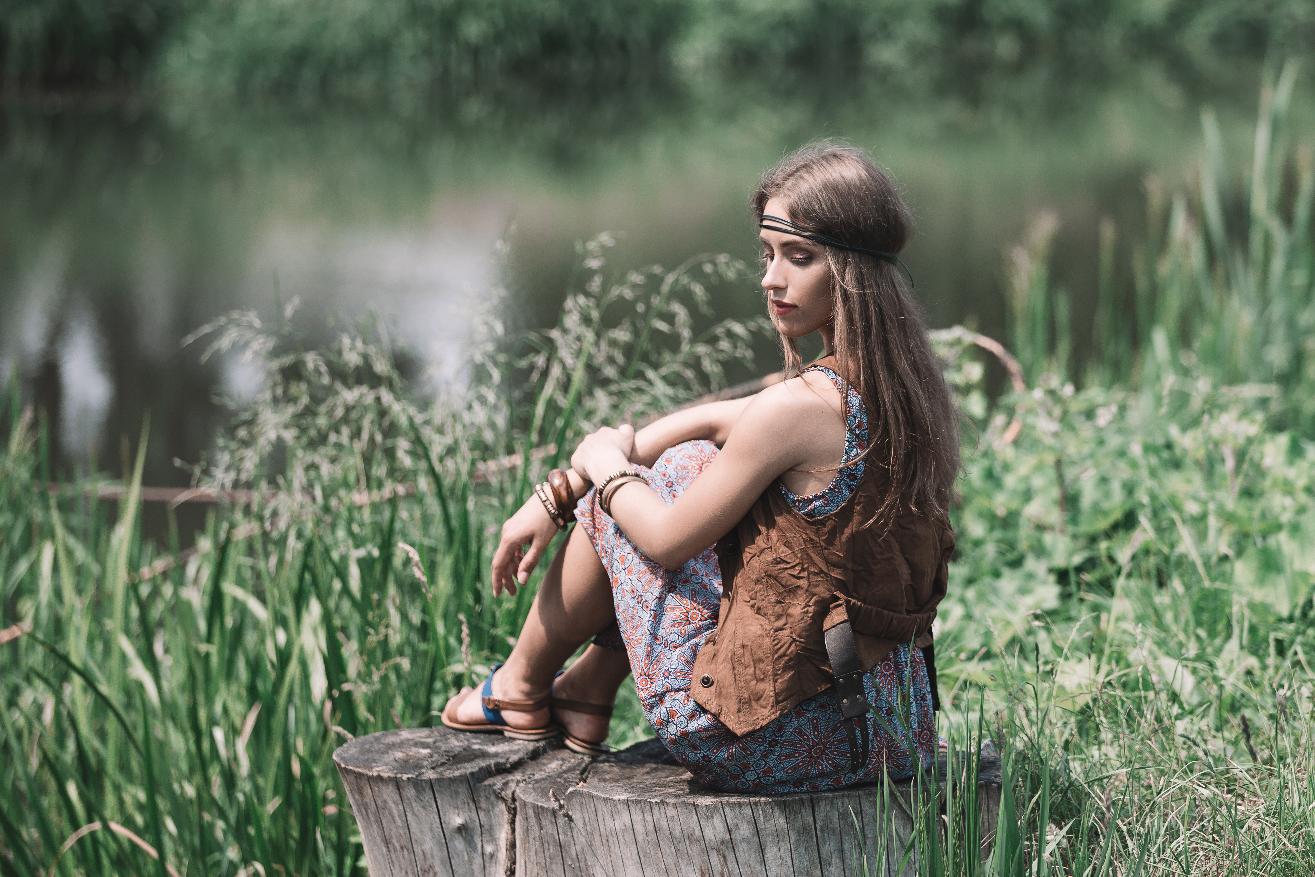 beautiful hippie girl sitting on a stump near the pond.