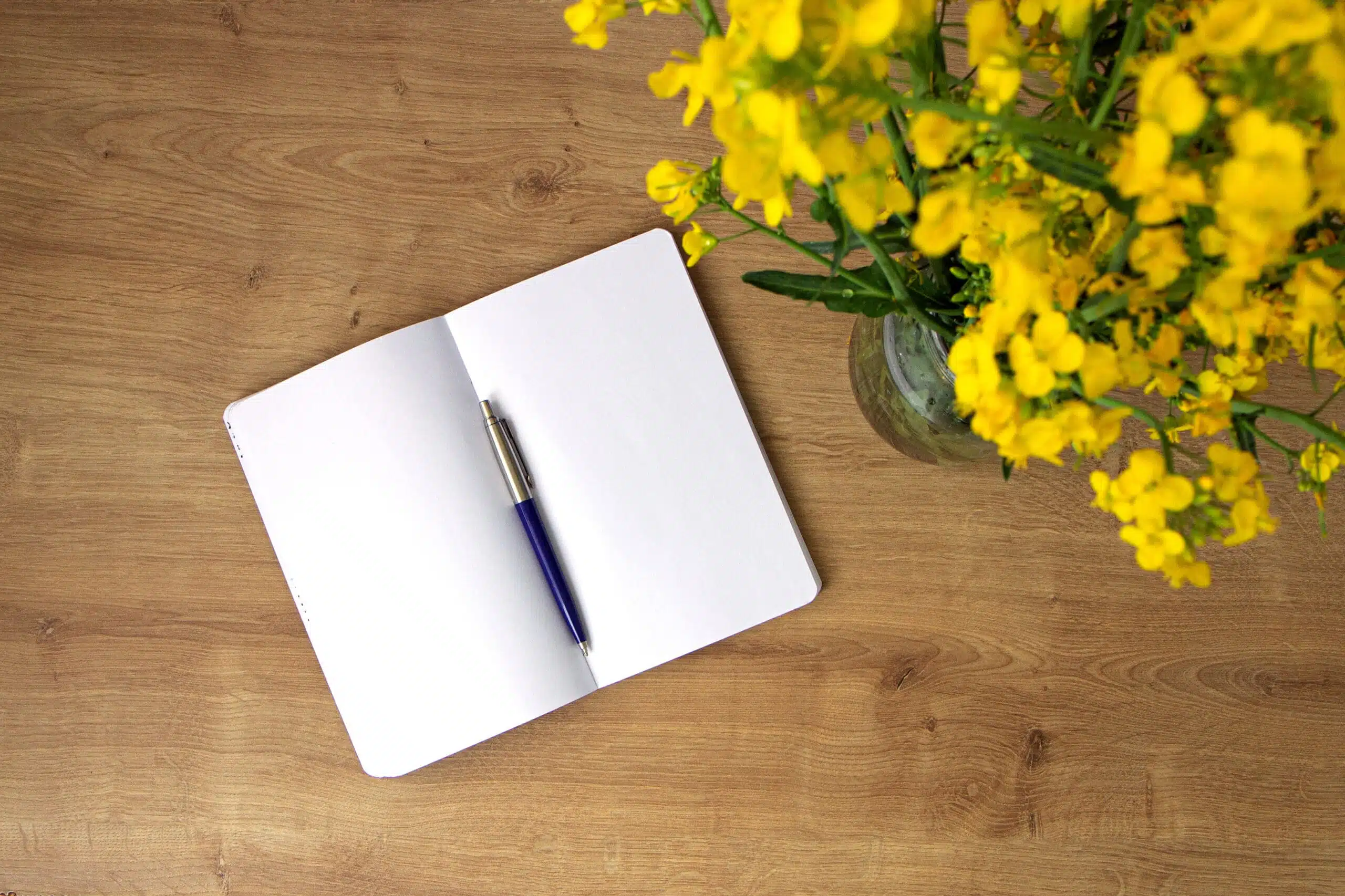 Open notebook with clean leaves with yellow flowers rapeseed on wooden table