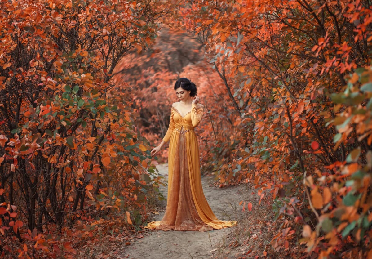 A fragile, tender girl in a yellow vintage dress strolls against the background of fiery autumn nature.