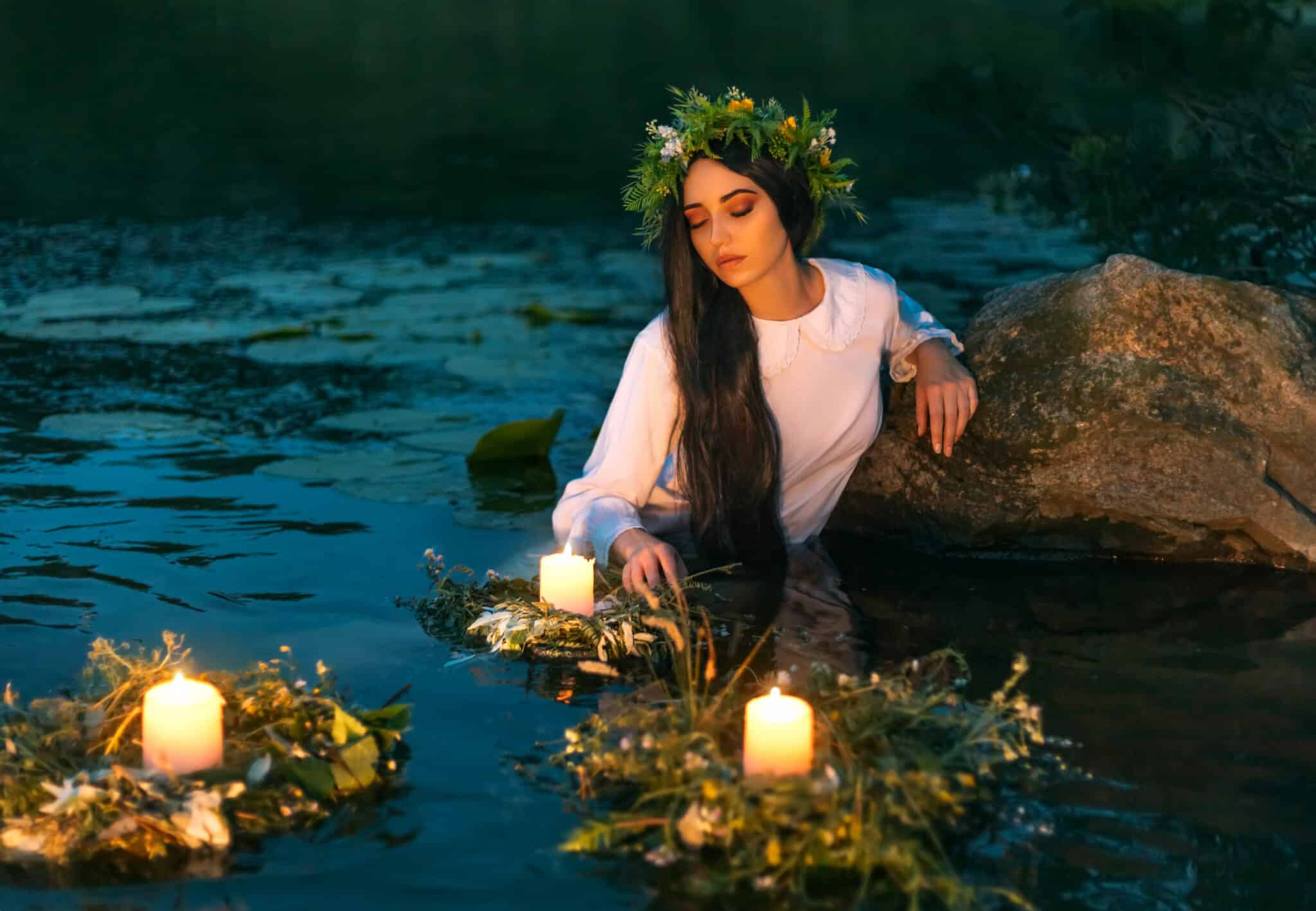 A nymph stands in water with floating wreath and candles burning