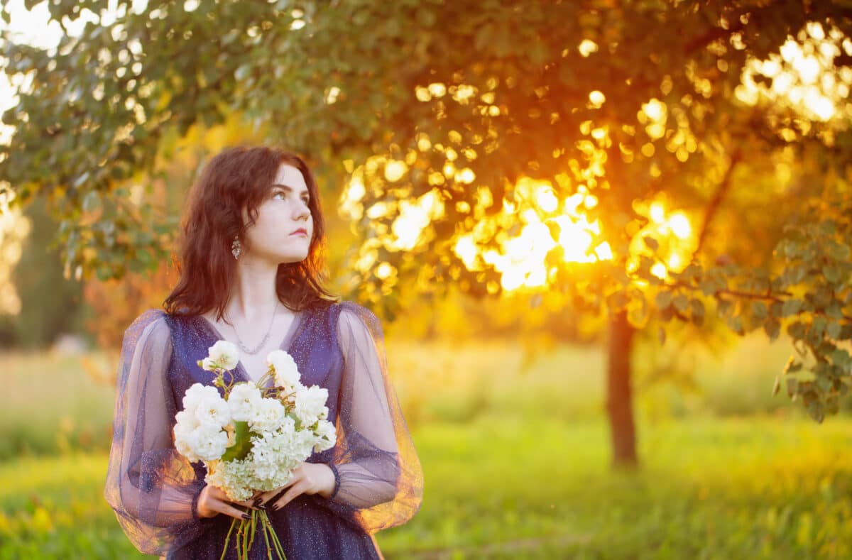 young beautiful woman in blue vintage dress with white flowers in nature at sunrise