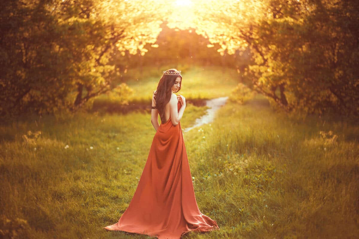 Beautiful young princess in a long red dress walks among the green plants in the woods , a fashionable toning , creative color