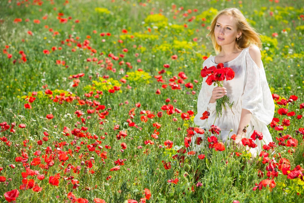 lady in white dress holding a bouquet of red poppy flowers in fields