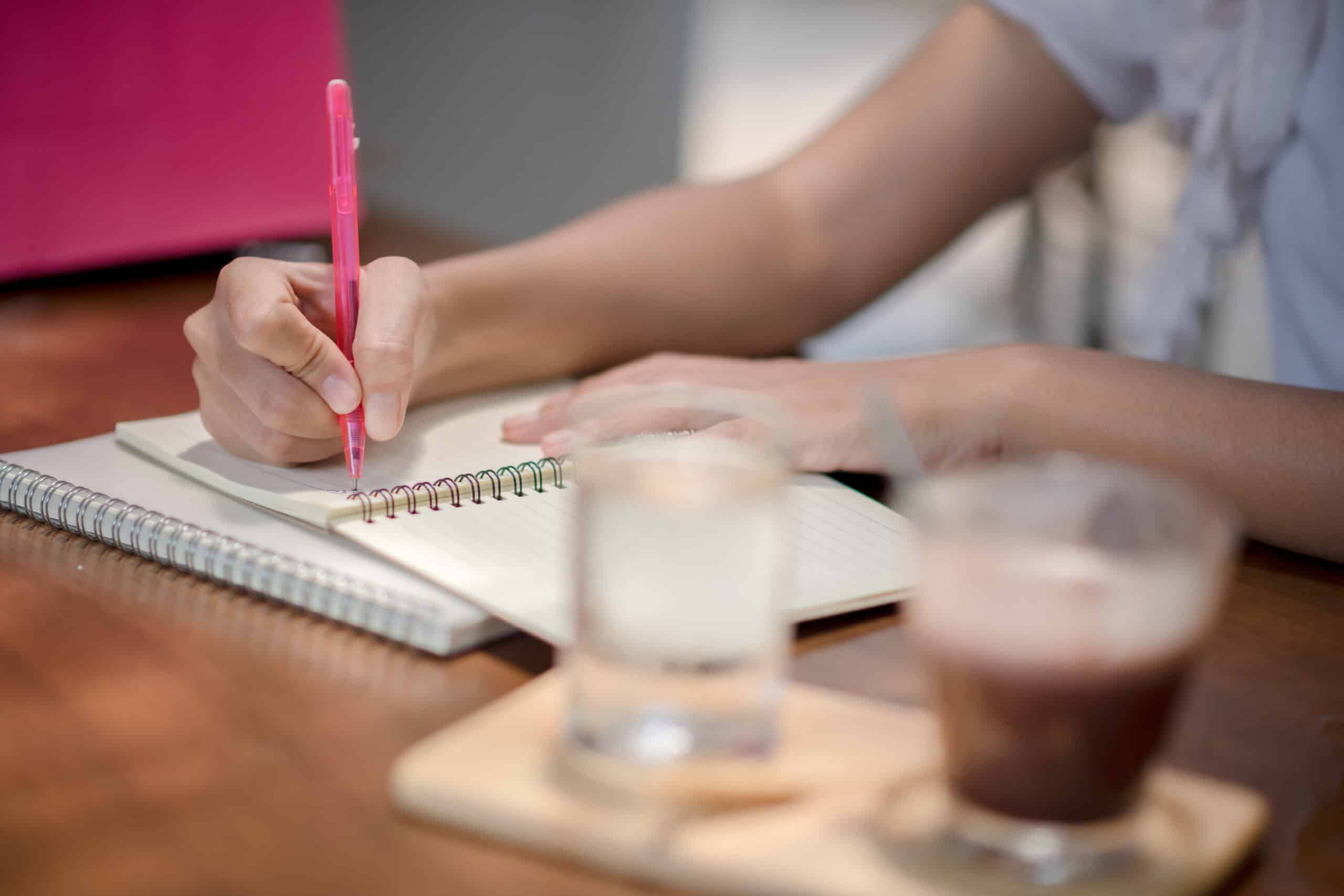 A woman writes with a pencil on a notebook at home.