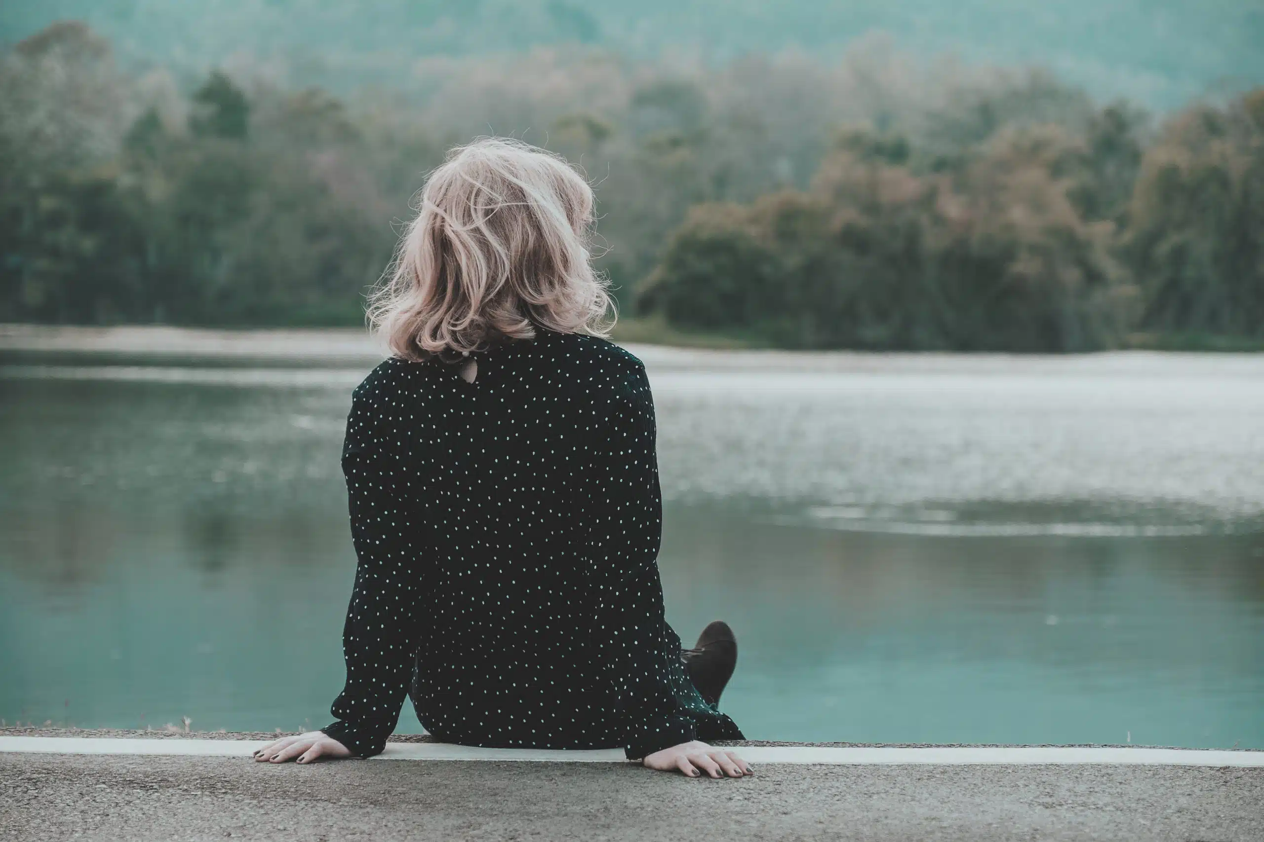 Girl sitting alone in the park on mountain looking at the lake
