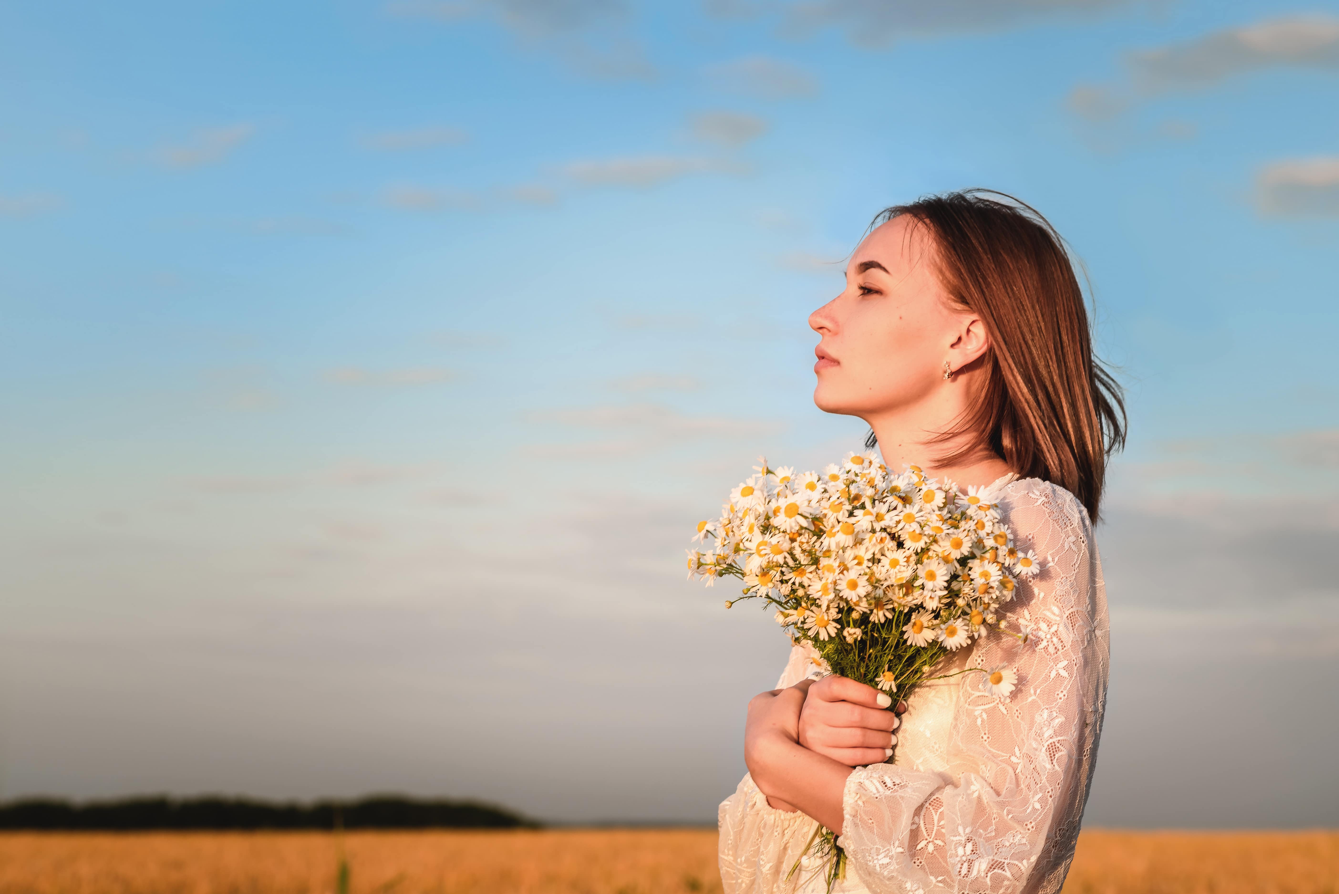 Beautiful woman in a white dress with a bouquet of flowers in a wheat field at sunset.