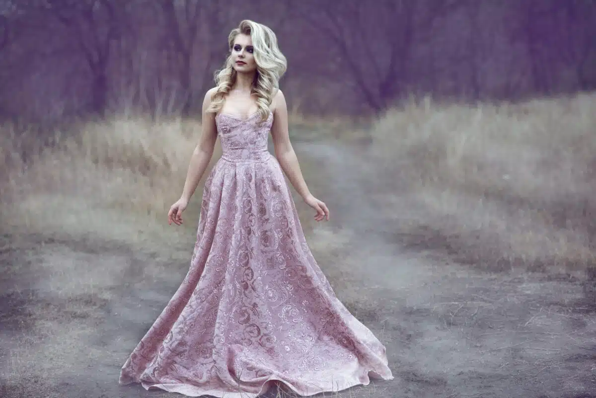 a gorgeous blond lady in a ball dress walking along the narrow path in the woods