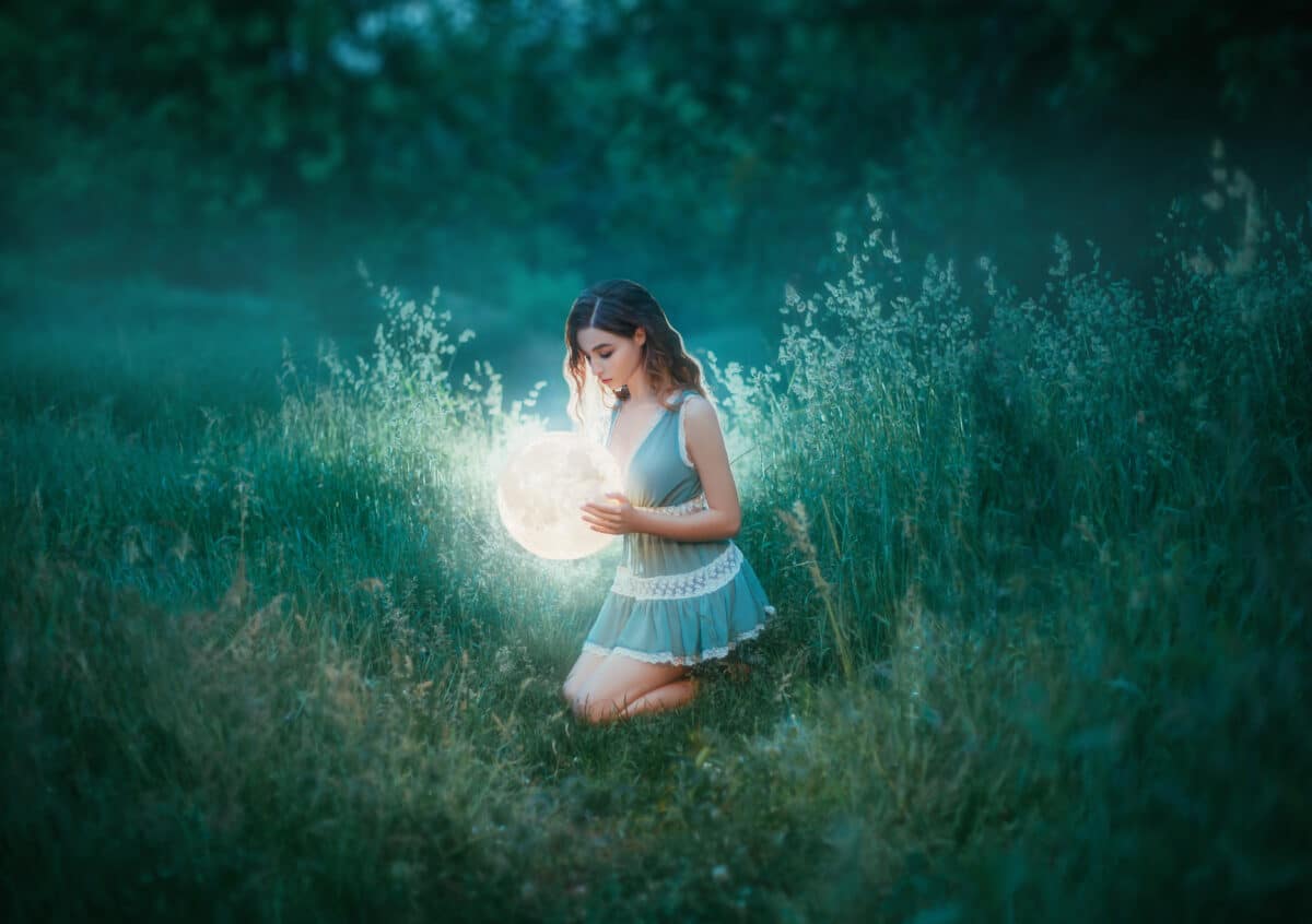 red haired witch. woman in blue green mint color short sexy dress, holds glow shining moon globe lamp. Casual fashion wear. Elf princess. Power of nature miracle. bright summer forest. Ball gold light