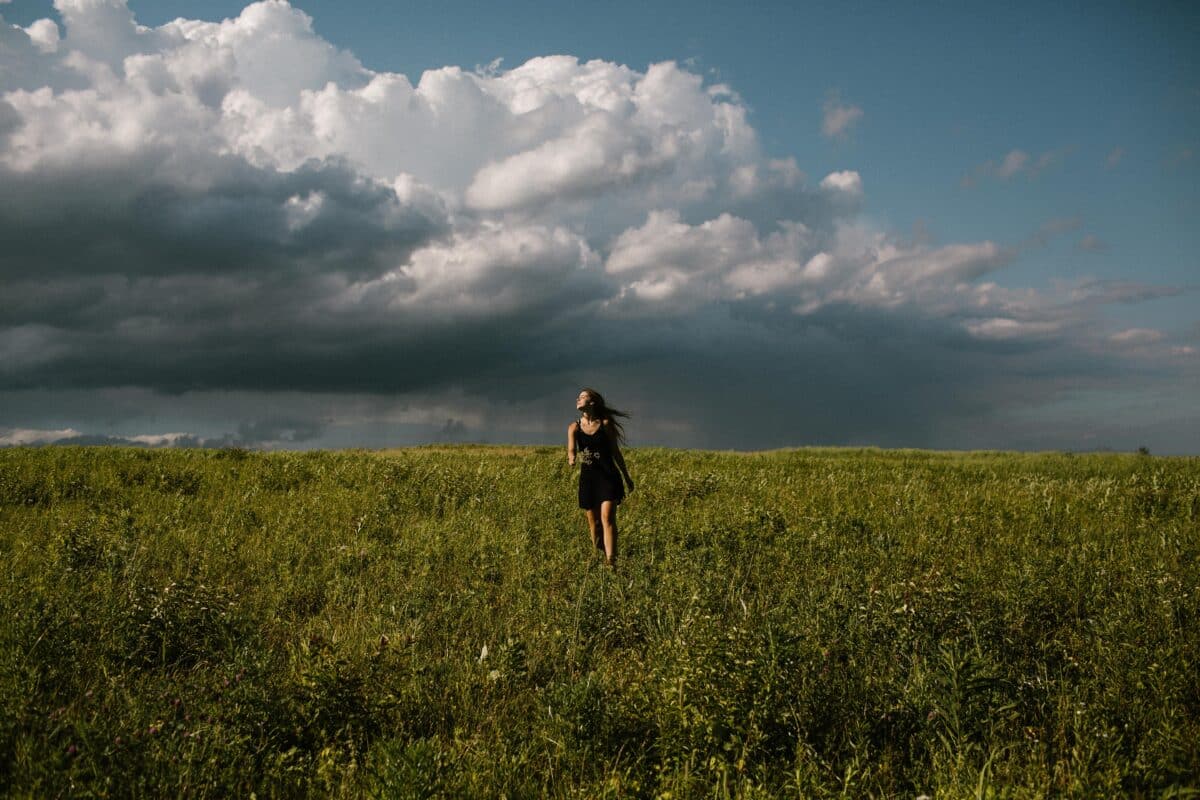 woman in a black dress running in a field with storm clouds in summer