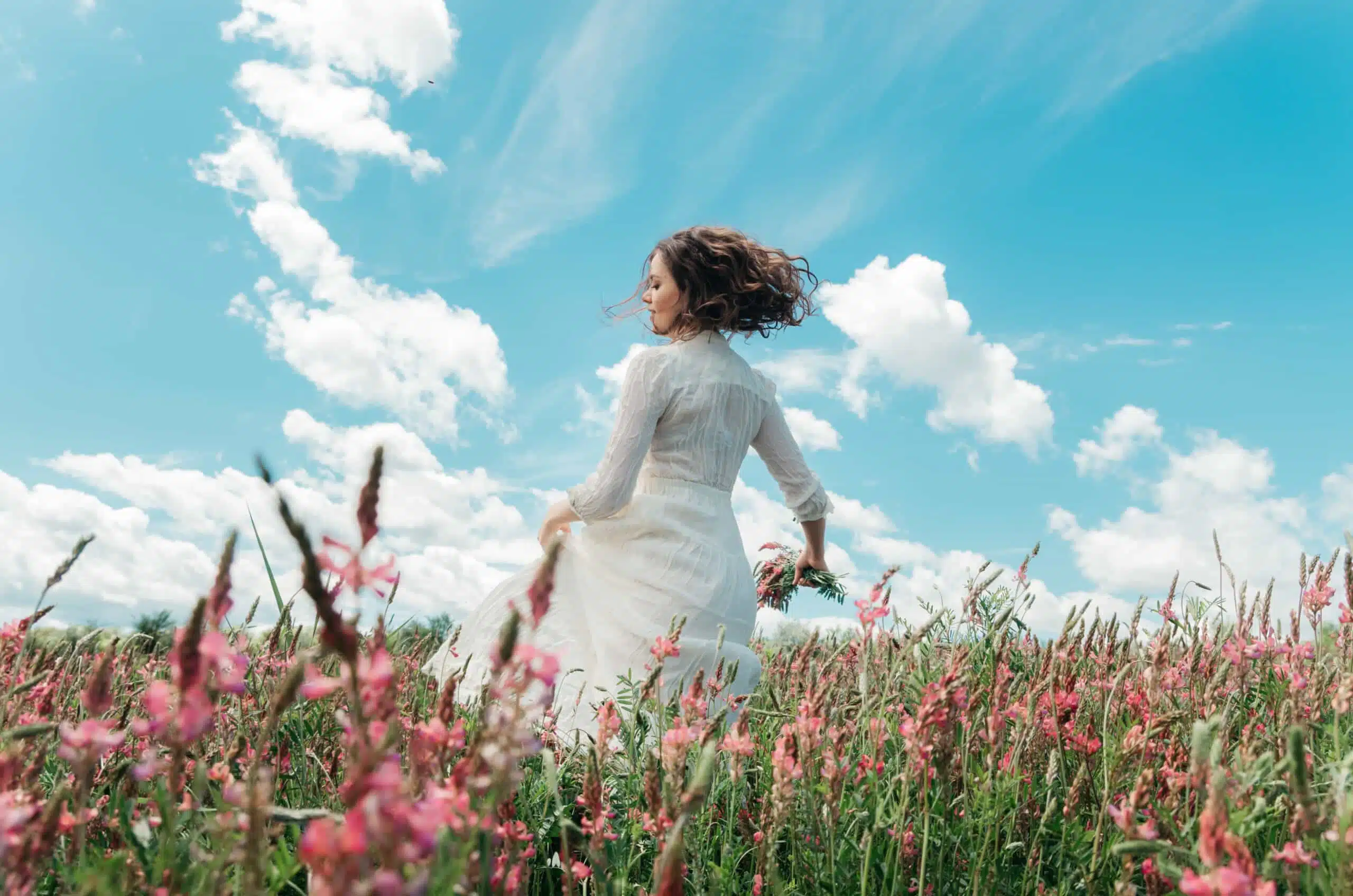 young woman in motion in a long white dress in a flower field.