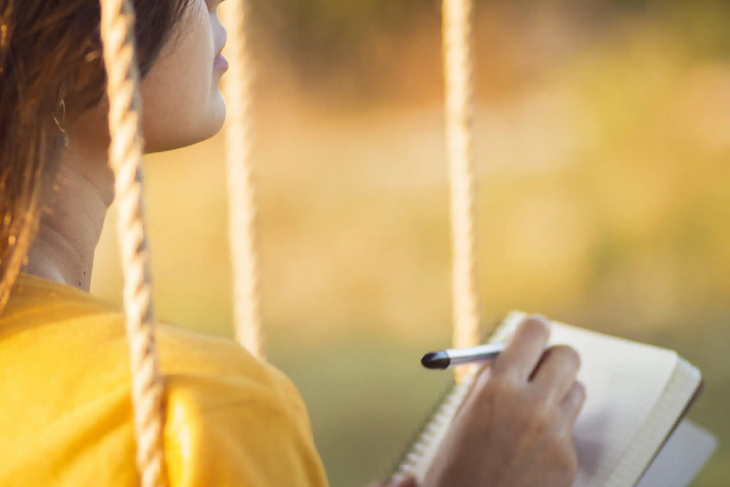 Young woman in pensive mood writing outdoors at a swing.