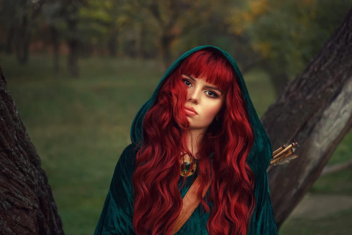 cute red-haired girl, looks into the camera with brown eyes, wearing an emerald raincoat with a hood on her head, has a leather quiver for arrows and an expensive shiny look on her neck. Gothic style