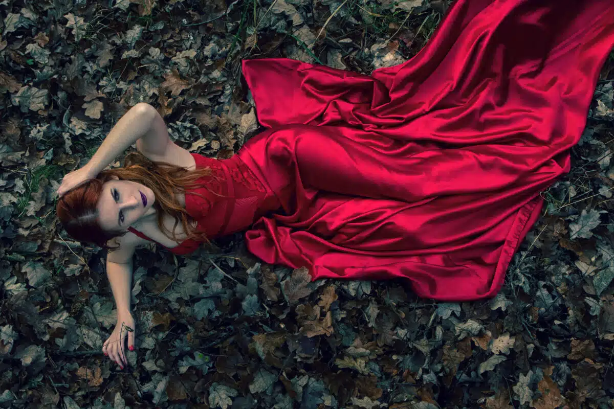 beautiful woman lie on a ground in red dress in the dark forest