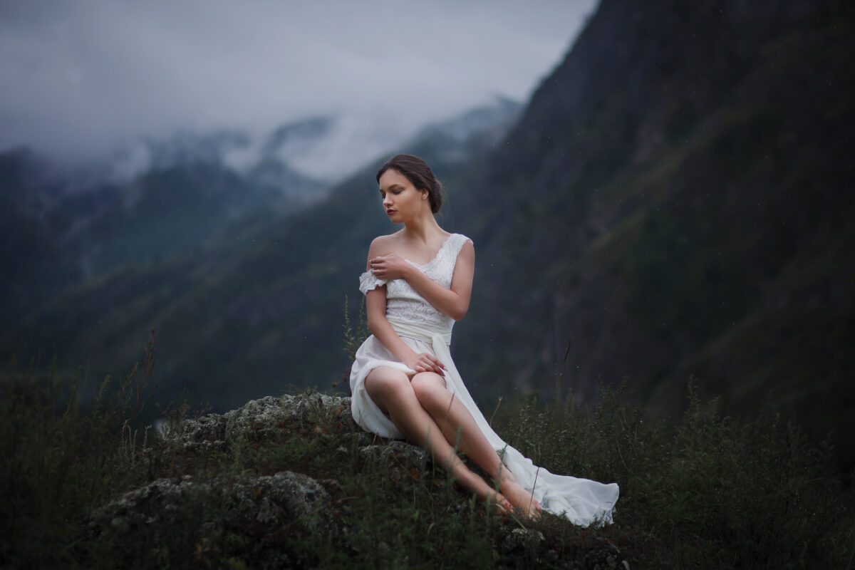 beautiful lady in white dress sitting on a rock on a foggy mountain