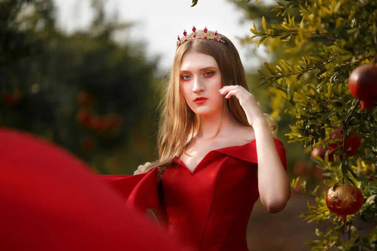 Beautiful young girl in long red dress in a pomegranate garden. Jewish New Year. Rosh Hashana concept