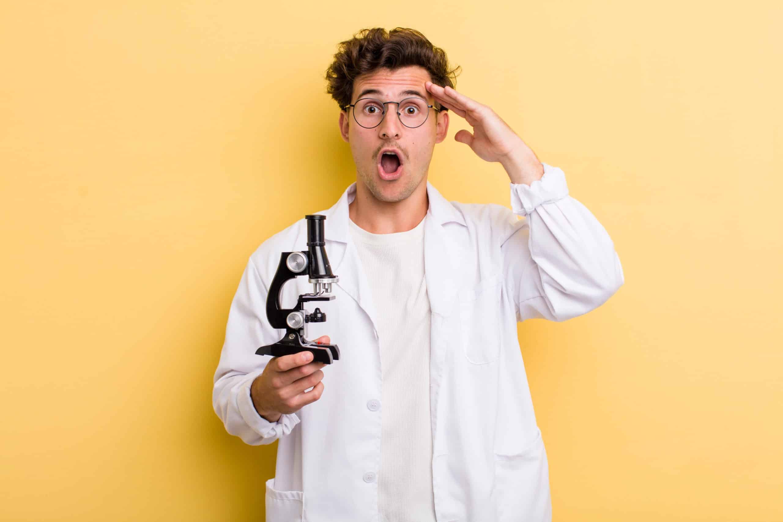 Young male scientist in a lab gown, looking happy and astonished.