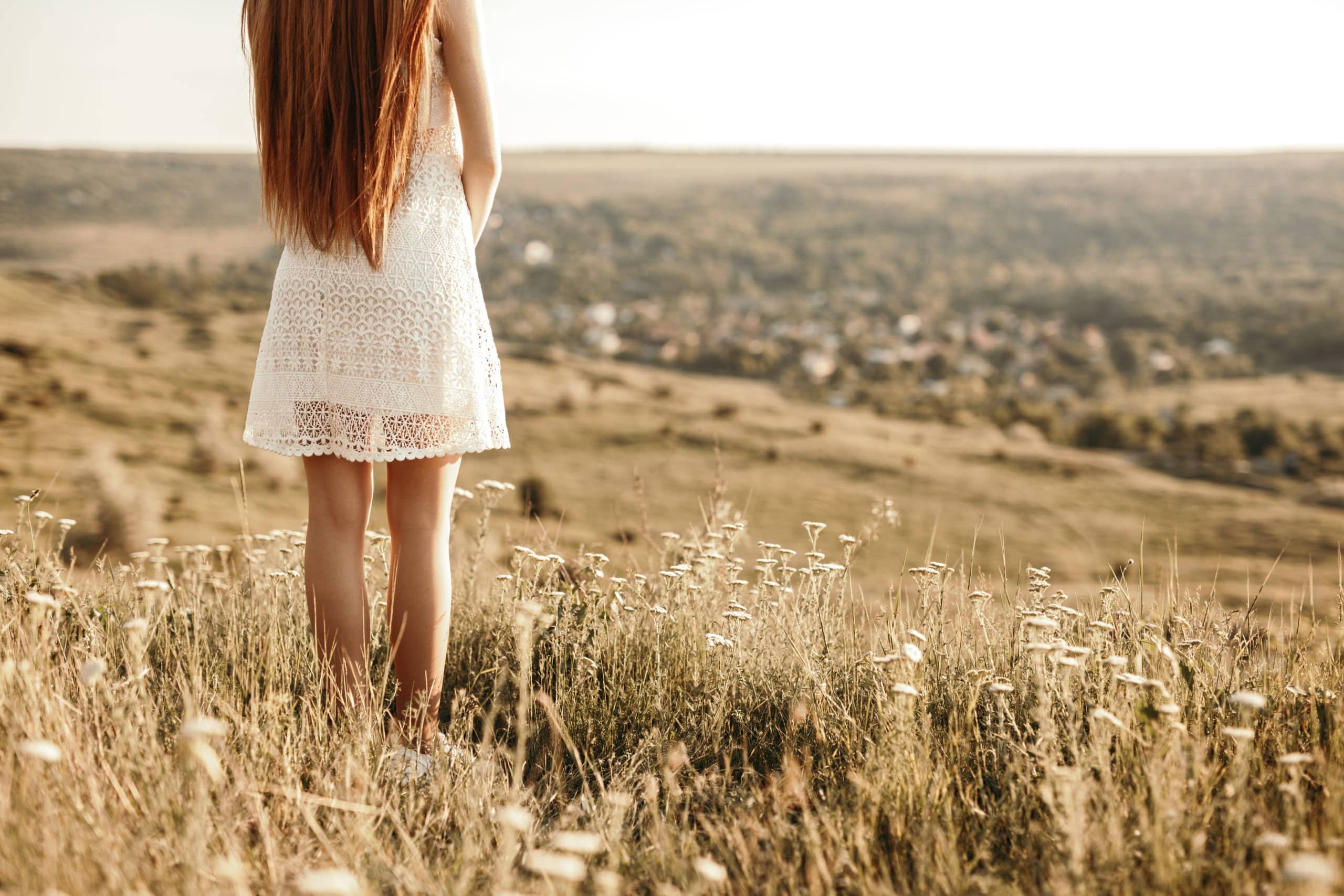 Lonely young woman in white dress standing in the field