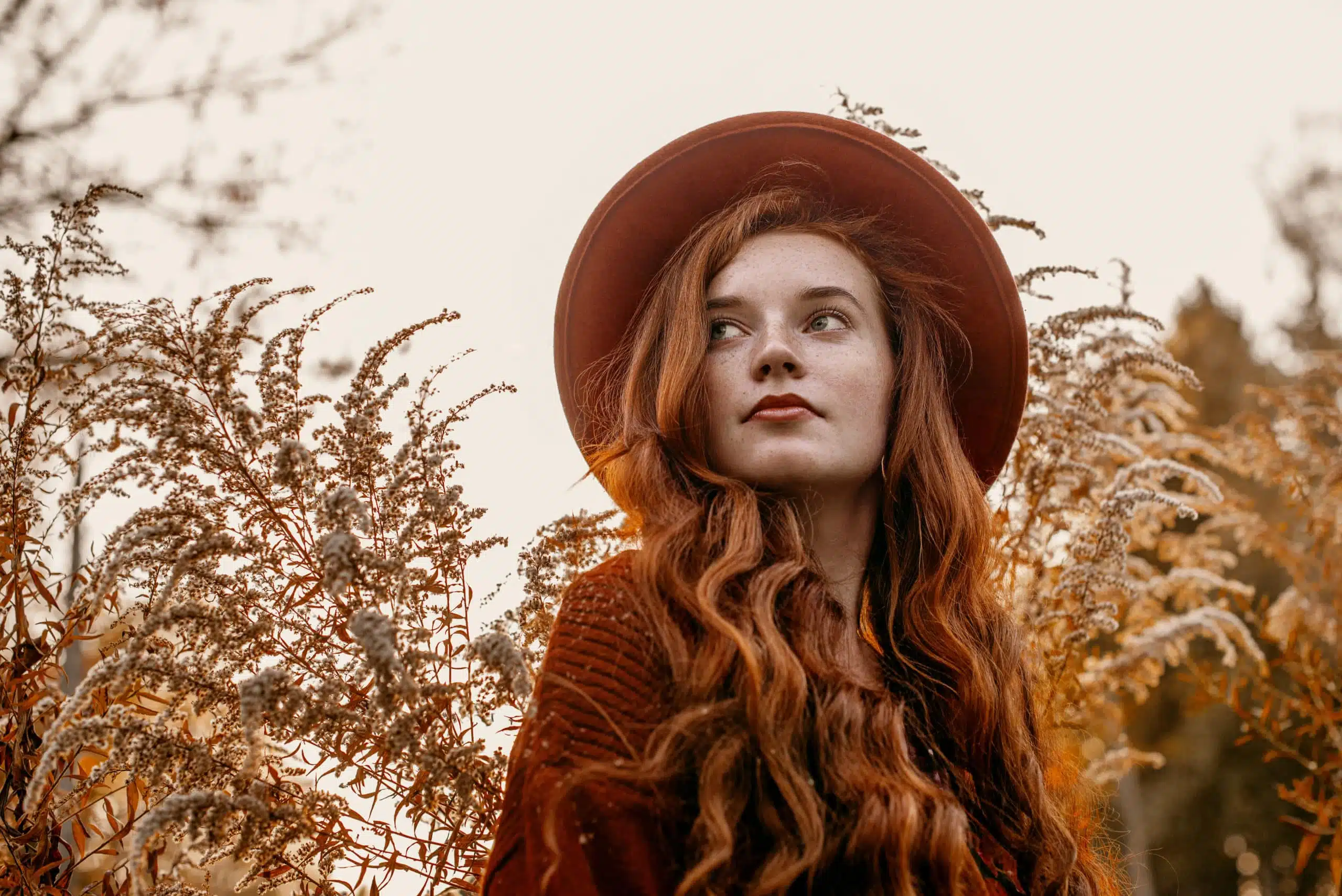 Young attractive redhead woman outdoors standing wearing a sun hat.
