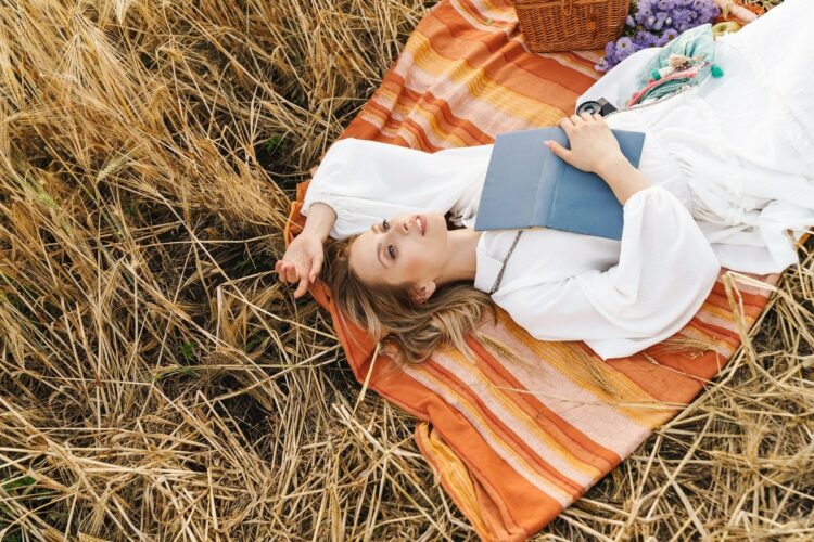 young blond woman lying on blanket with book in golden