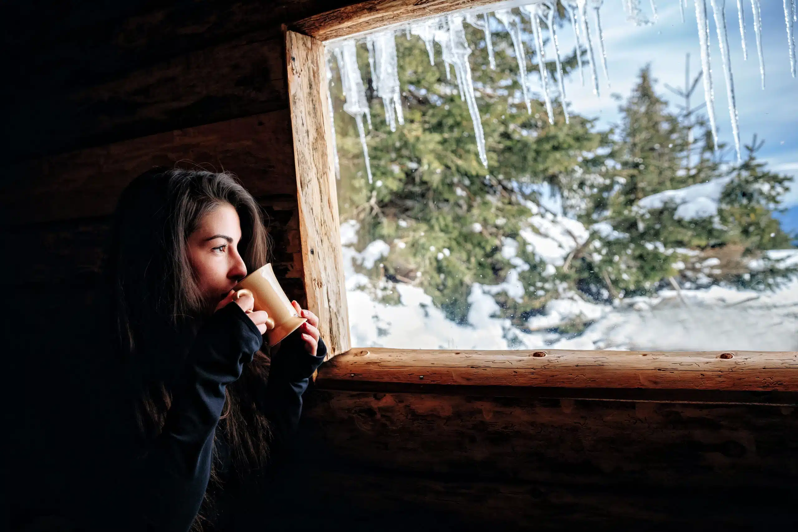 woman with a mug of tea looks out of the window in winter