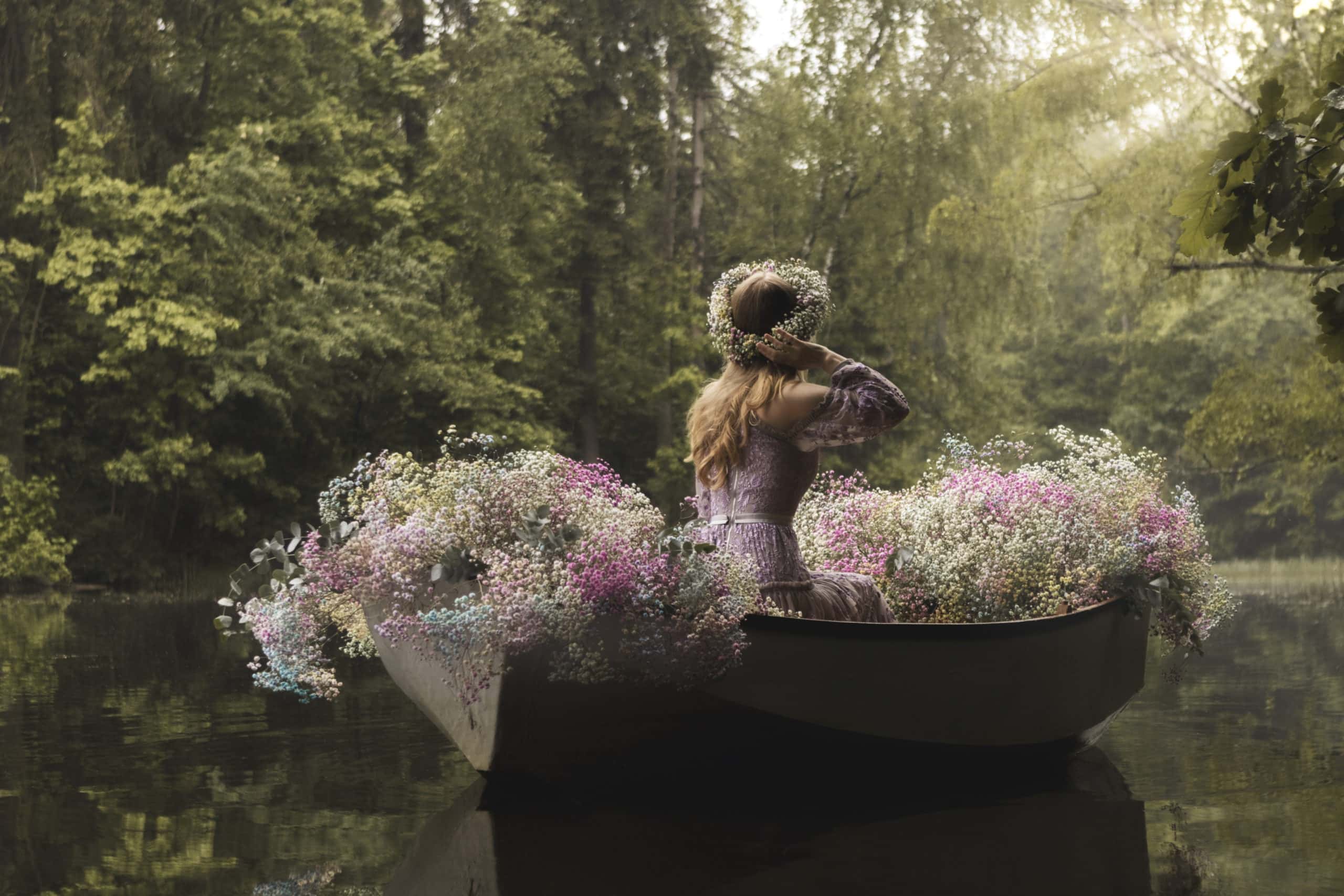 Woman in a boat decorated with flowers floats on the lake in the forest.