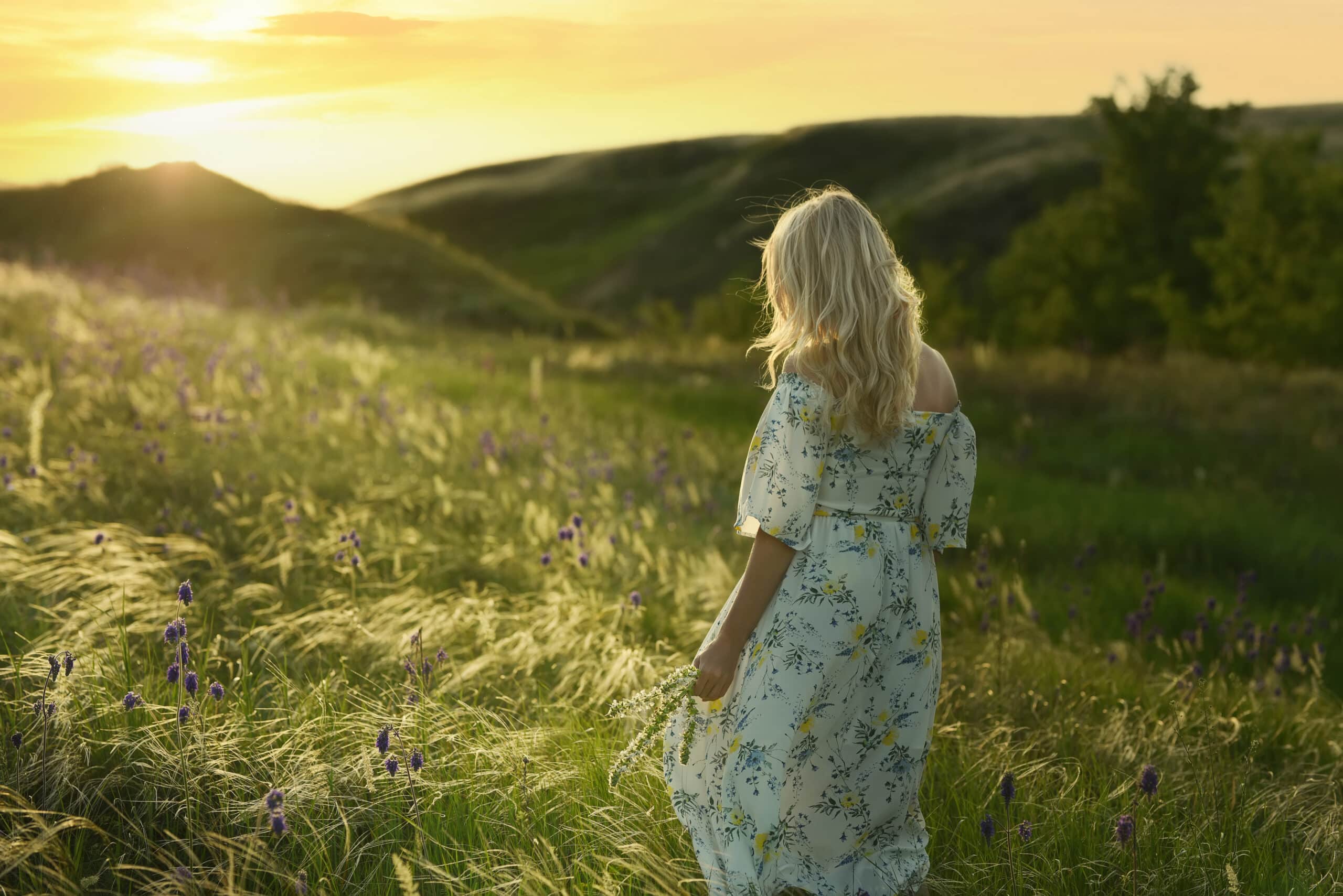 A woman in a spring summer field at sunset picking flowers