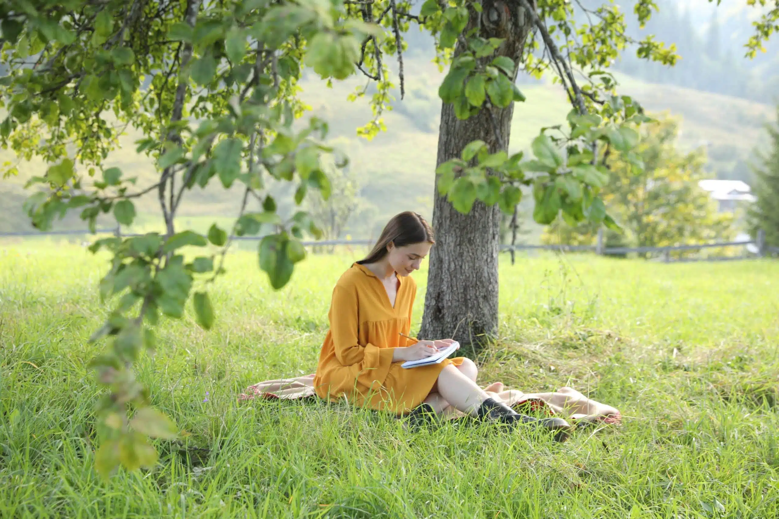Beautiful young woman writing in notepad outdoor on the grass.