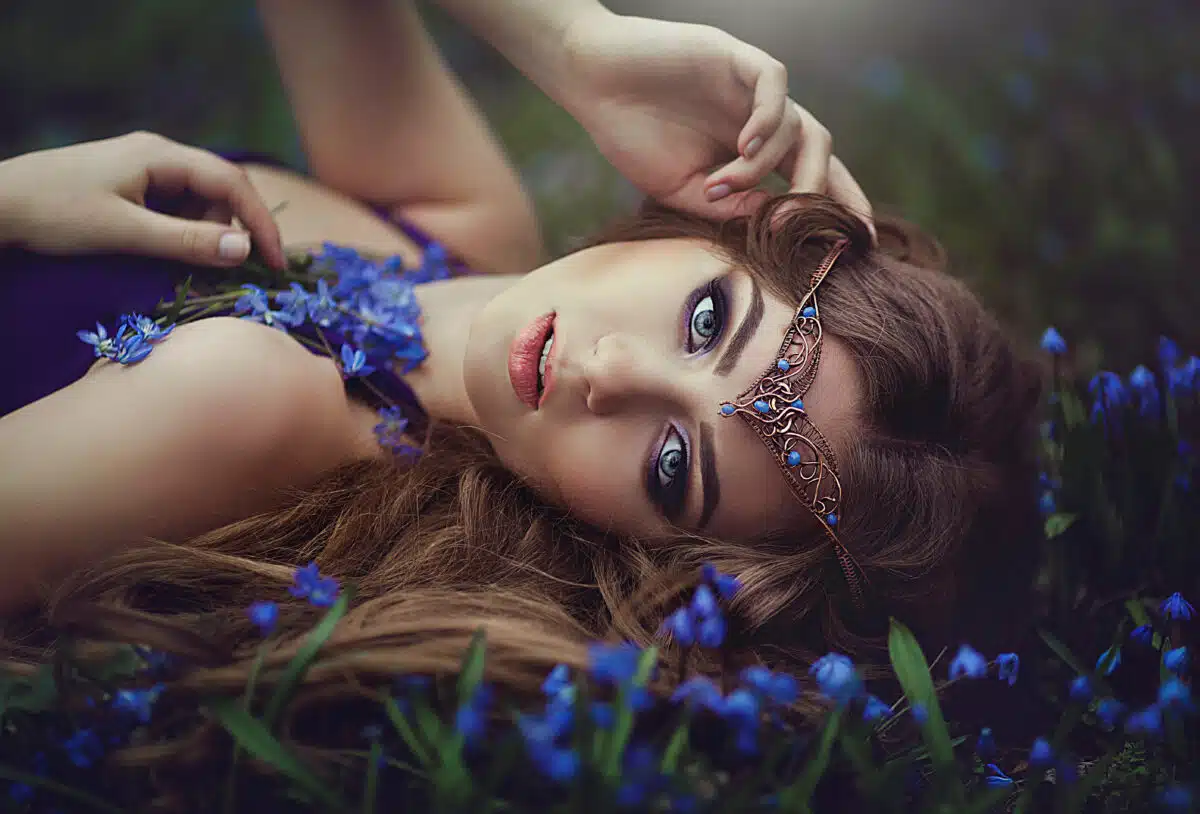 a princess with long hair and blue eyes wearing a tiara rests in spring forest blue forest flowers
