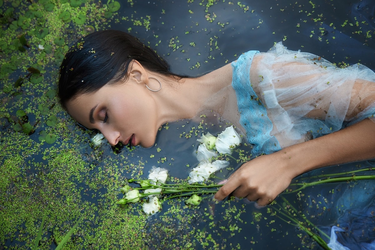beautiful romantic woman lies in swamp in blue long dress with flowers. 