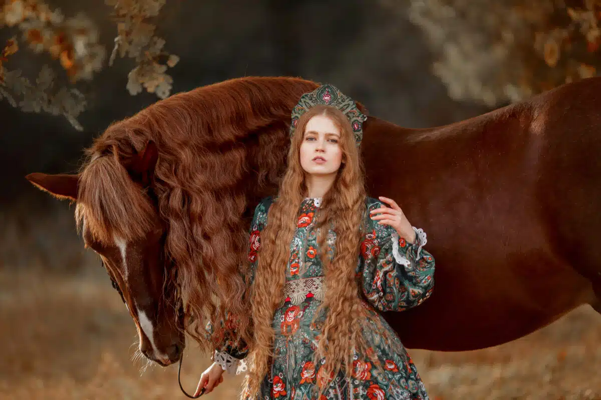 enchanting long-haired blonde lady wearing a diadem standing with her horse outdoor