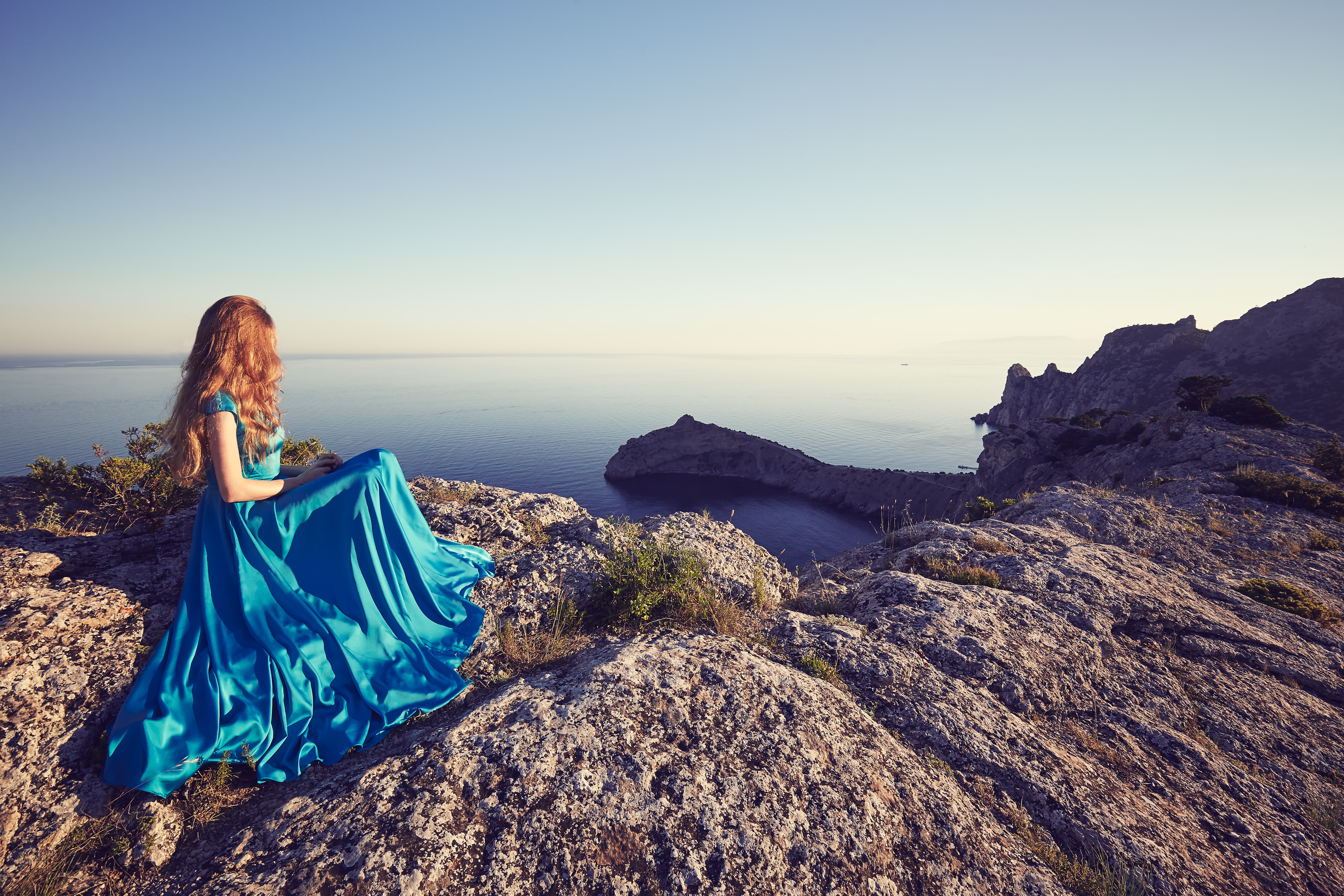 Young beautiful woman in blue dress on top of a mountains looking out to sea