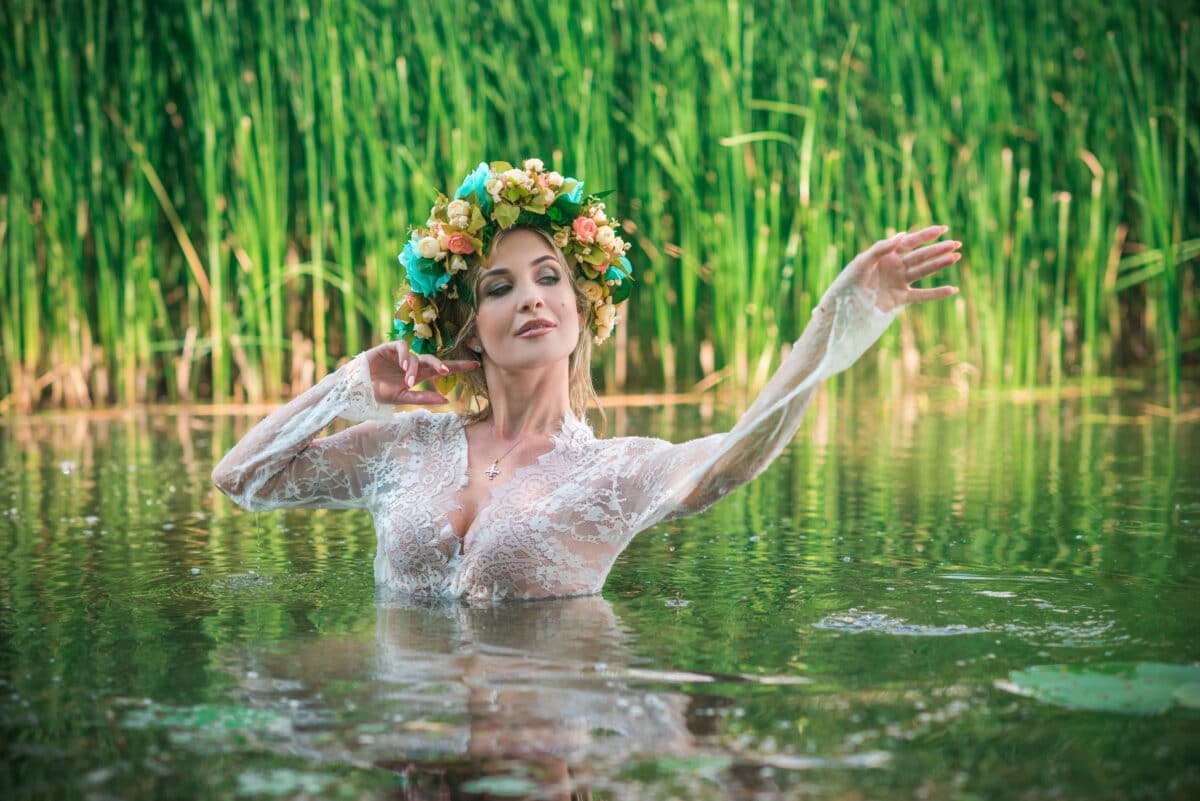 a lake nymph in long white lace dress and wreath playing in the water