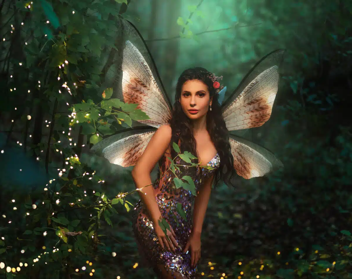 Portrait fantasy woman fairy, pixie wings creative costume. Girl angel forest goddess butterfly sexy elf. Magic light dark wood landscape night, trees fireflies, magic glow. Pink sparkle shining dress