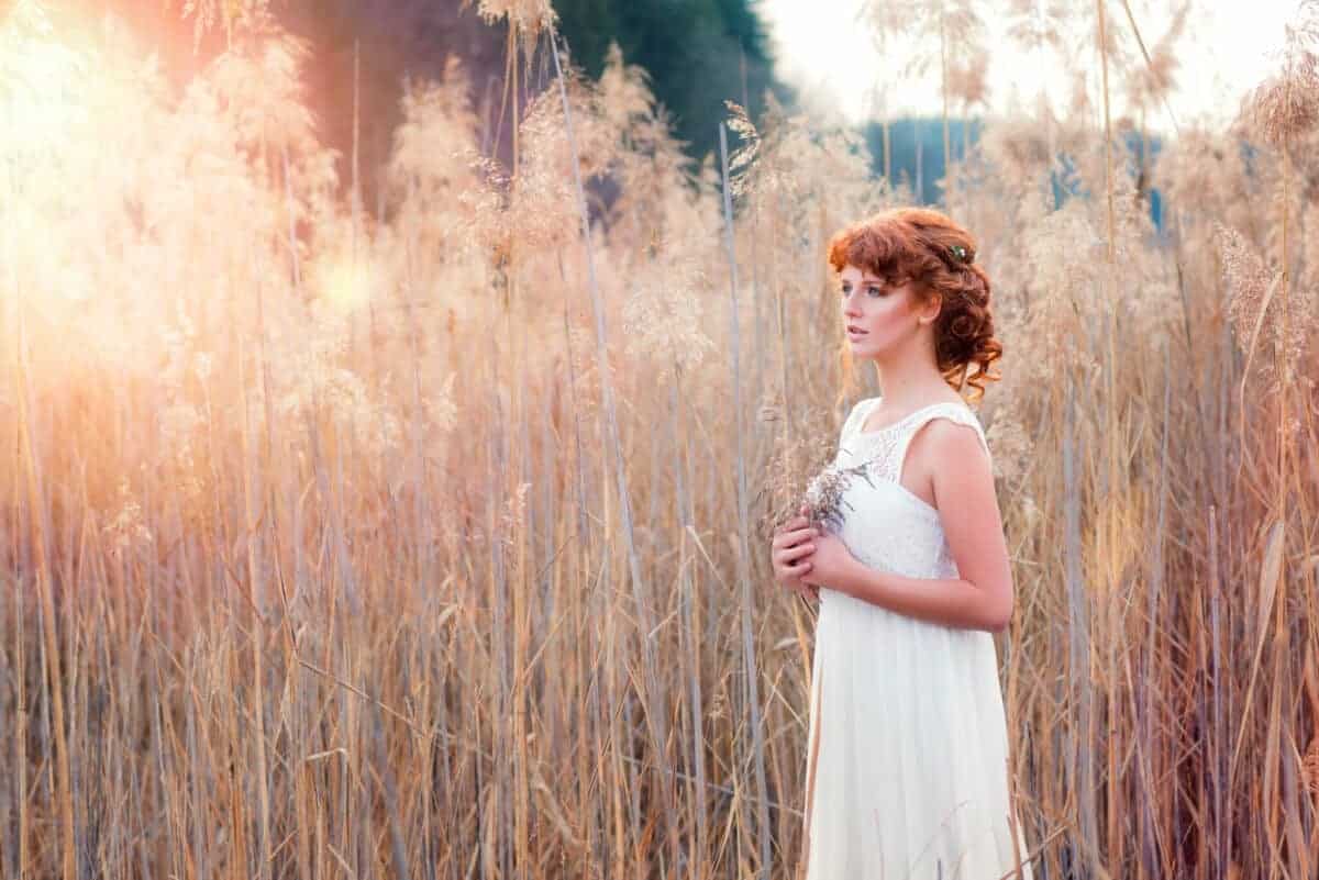 young princess with a longing expression holding a flower while standing in the field of tall grasses