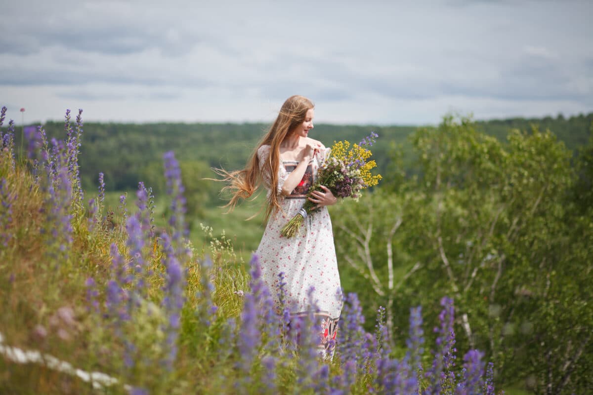Medieval lady in historical dress collects summer wild flowers on sunny day