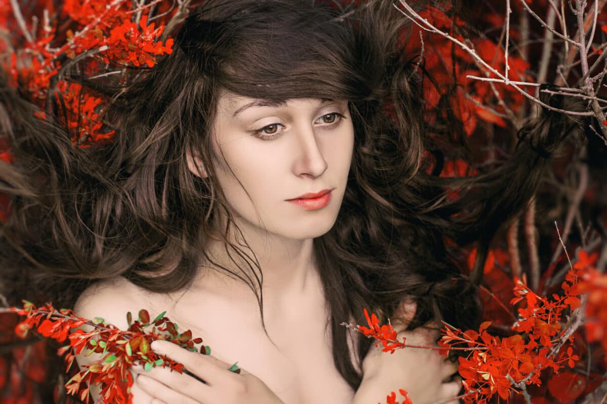 mysterious woman lying in the branches with red leaves in the forest
