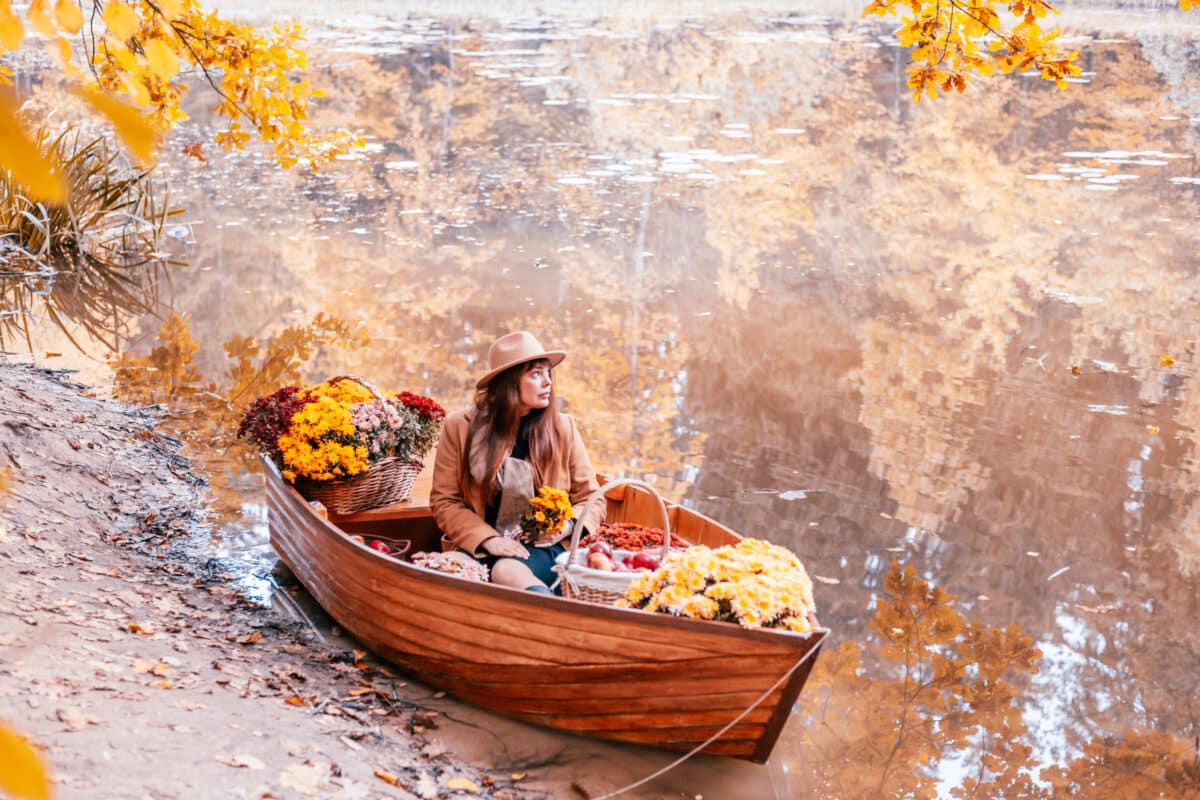 a beautiful woman sitting in boat with flowers on the pond in autumn