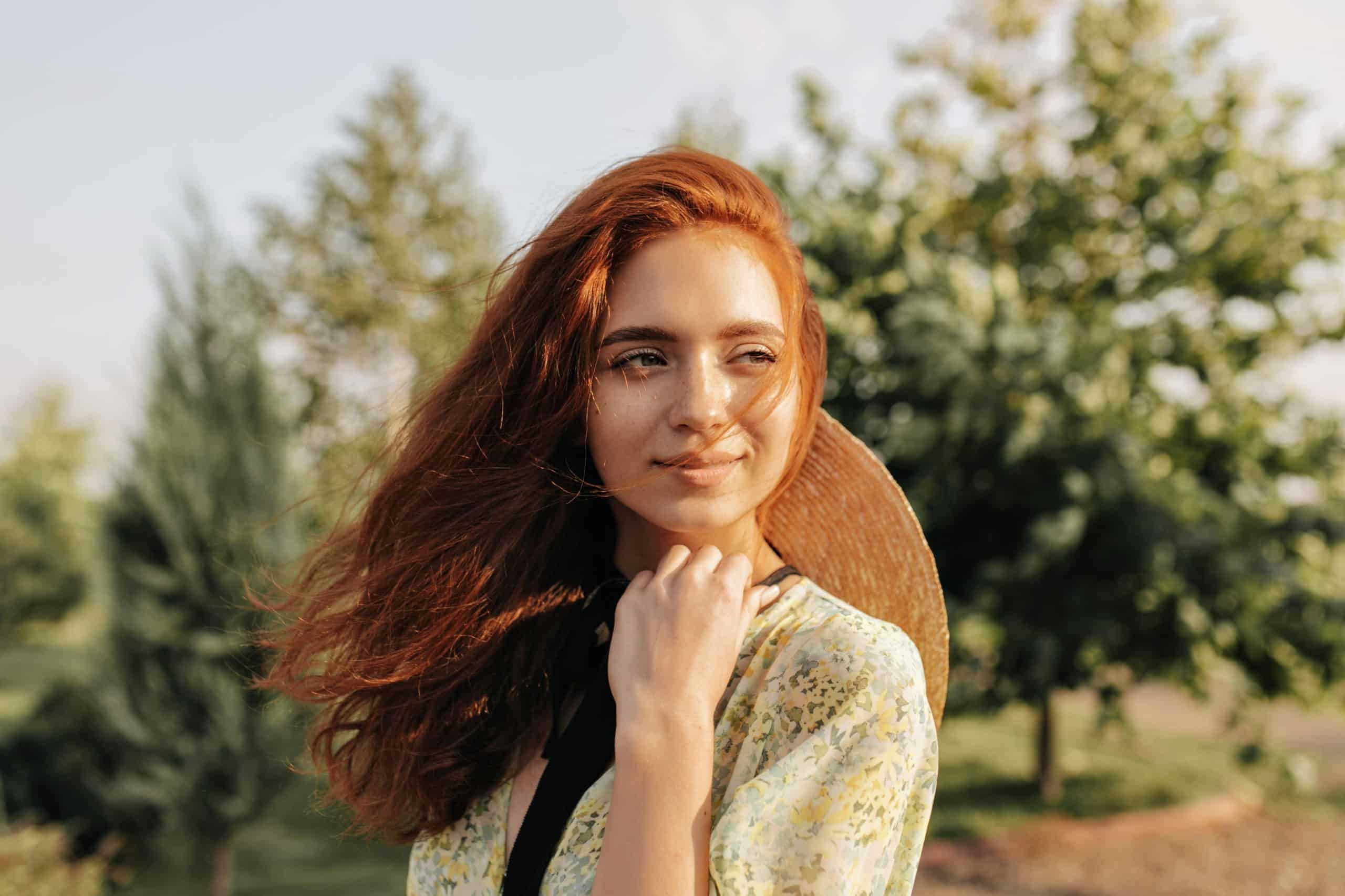Red haired young woman with cute freckles and brown eyes smiling and looking away outdoor.