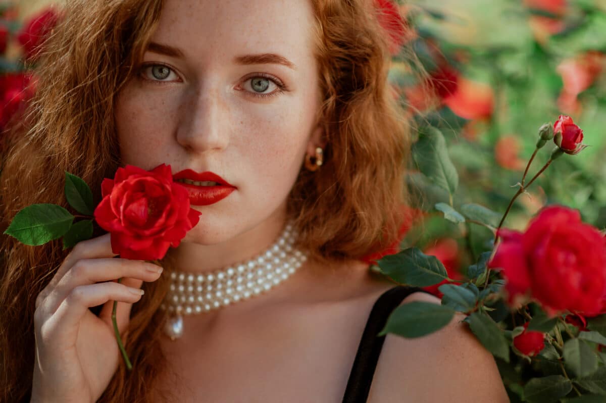 female redhead kissing a rose in the garden